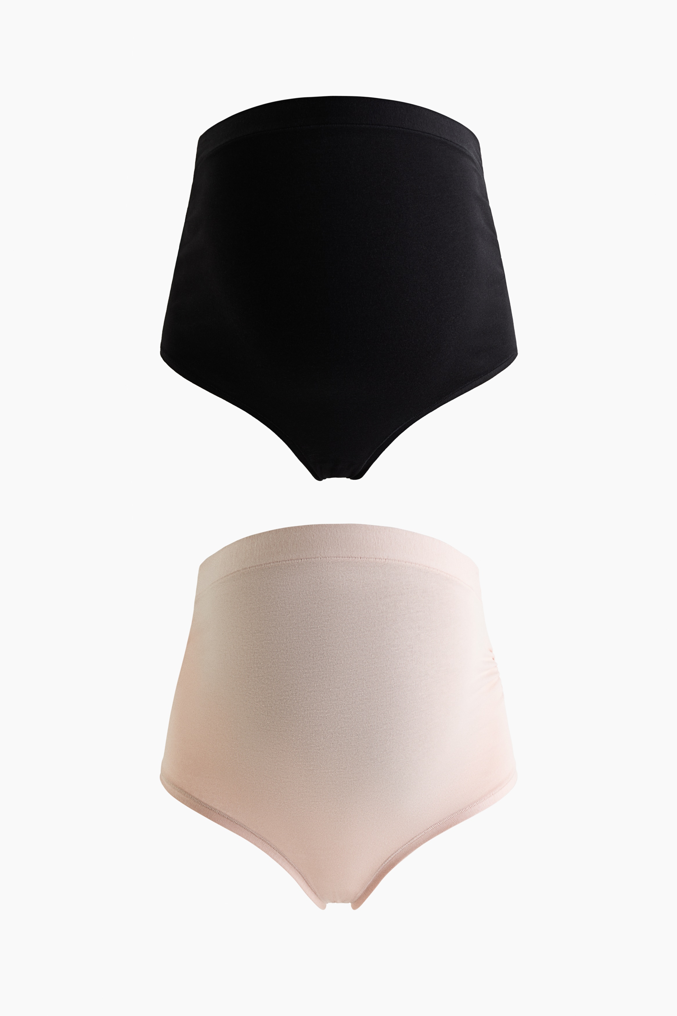 High-waisted black briefs featuring gathered side seams are being worn by the model while kneeling. The briefs are styled with a matching black bralette featuring lace trim along the neckline.