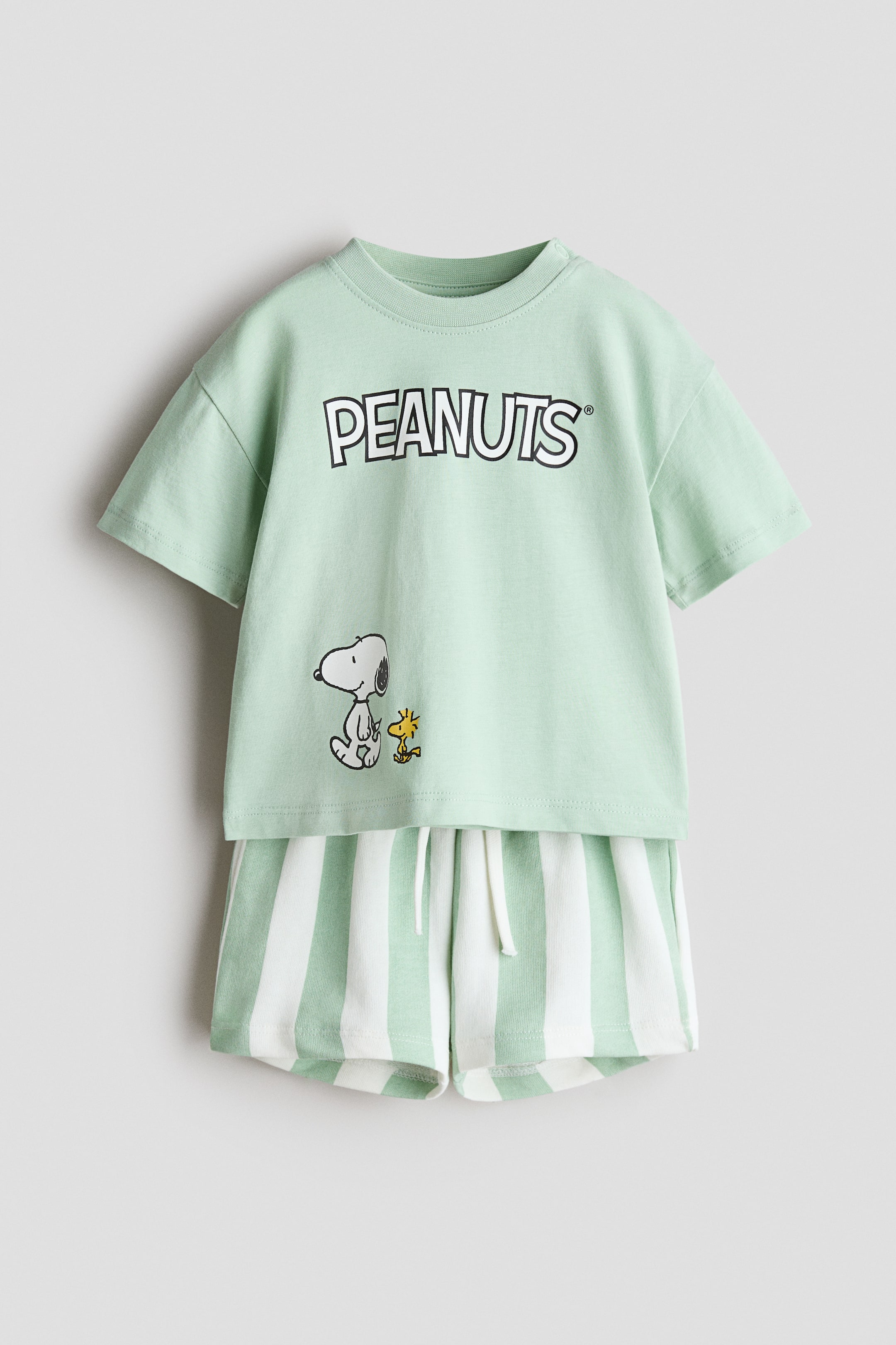 View larger image: This 2-piece printed set features a light green short-sleeved t-shirt with a crew neck, adorned with a 'PEANUTS' graphic and an illustration of Snoopy and Woodstock. It is paired with light green and white vertically striped shorts, complete with a visible white drawstring.