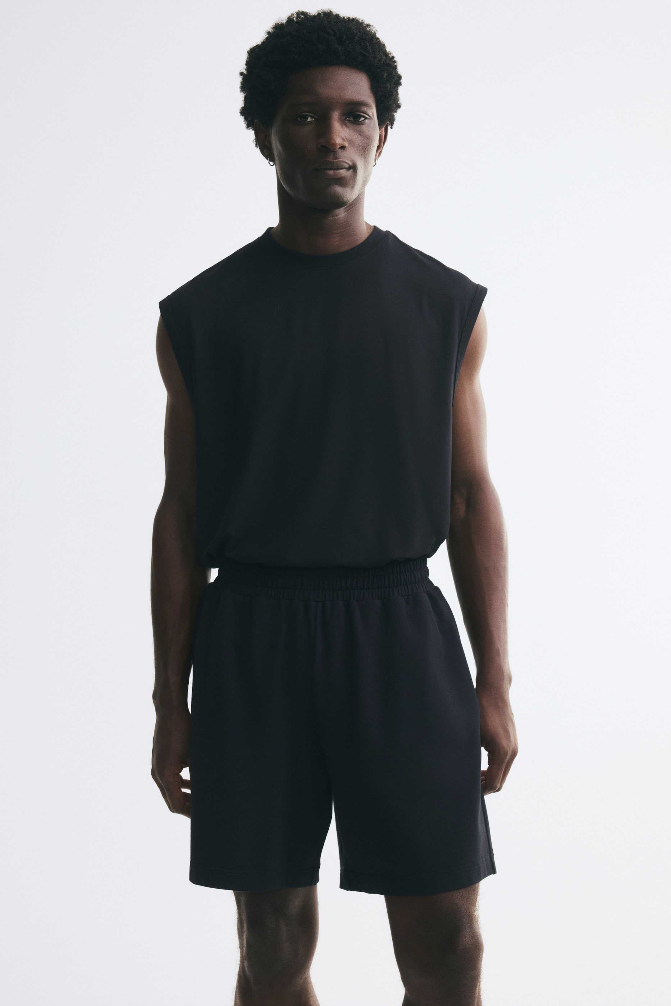 View larger image: Dark sweat shorts with a gathered elastic waistband and a regular fit are worn by the model. The shorts are styled with a matching sleeveless top tucked into the waistband.