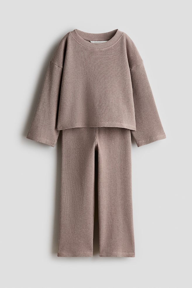 Ensemble de détente en maille gaufrée deux pièces présenté de face, comprenant un haut à col rond avec des épaules tombantes et des manches larges, assorti à un pantalon large, le tout dans une teinte taupe douce. - 1