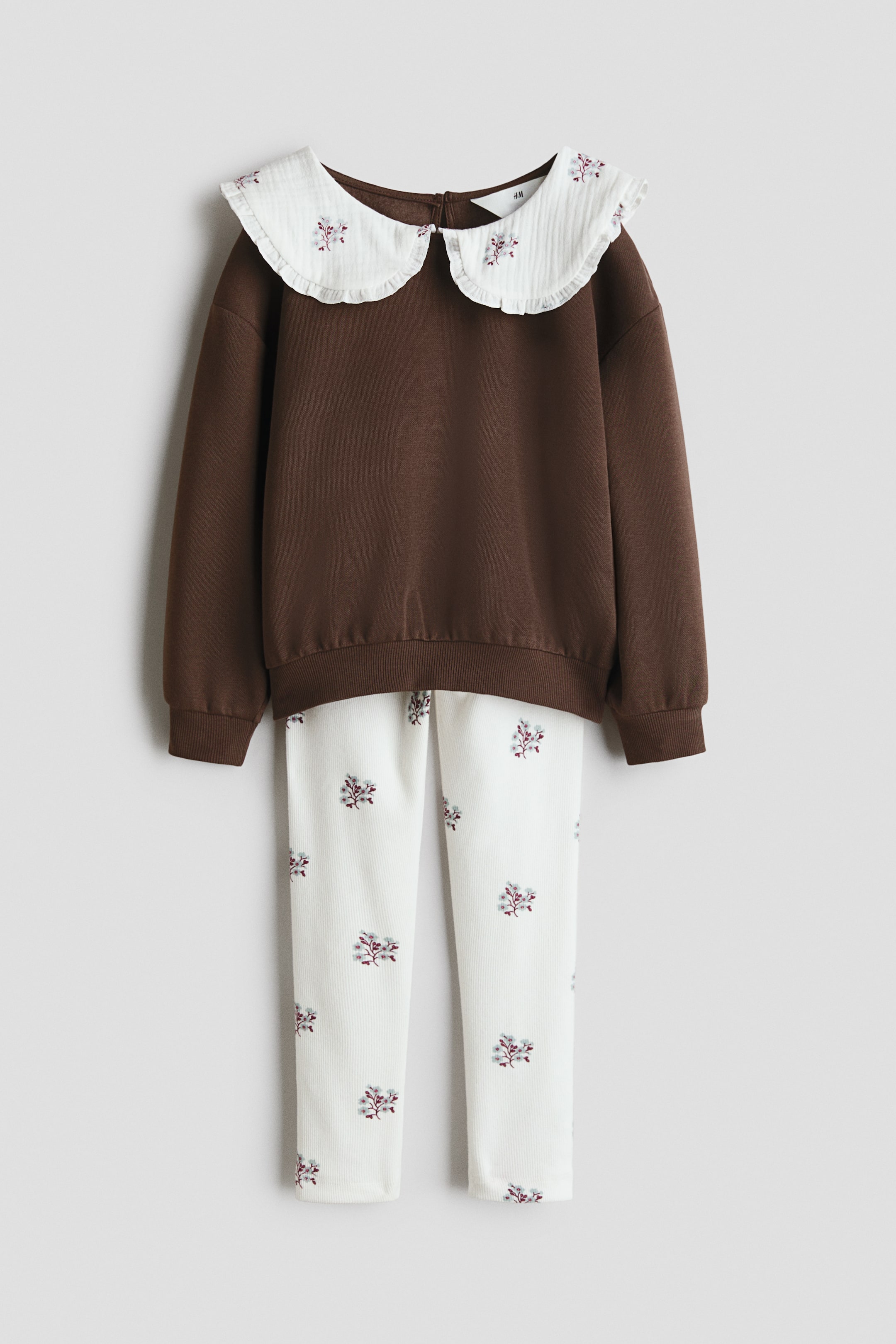 View larger image: A two-piece outfit is shown from the front, consisting of a brown long-sleeved sweatshirt and white ribbed leggings. The sweatshirt features a white ruffled Peter Pan collar with delicate floral embroidery, along with ribbed cuffs and a ribbed hem, while the leggings display an allover matching floral embroidery.
