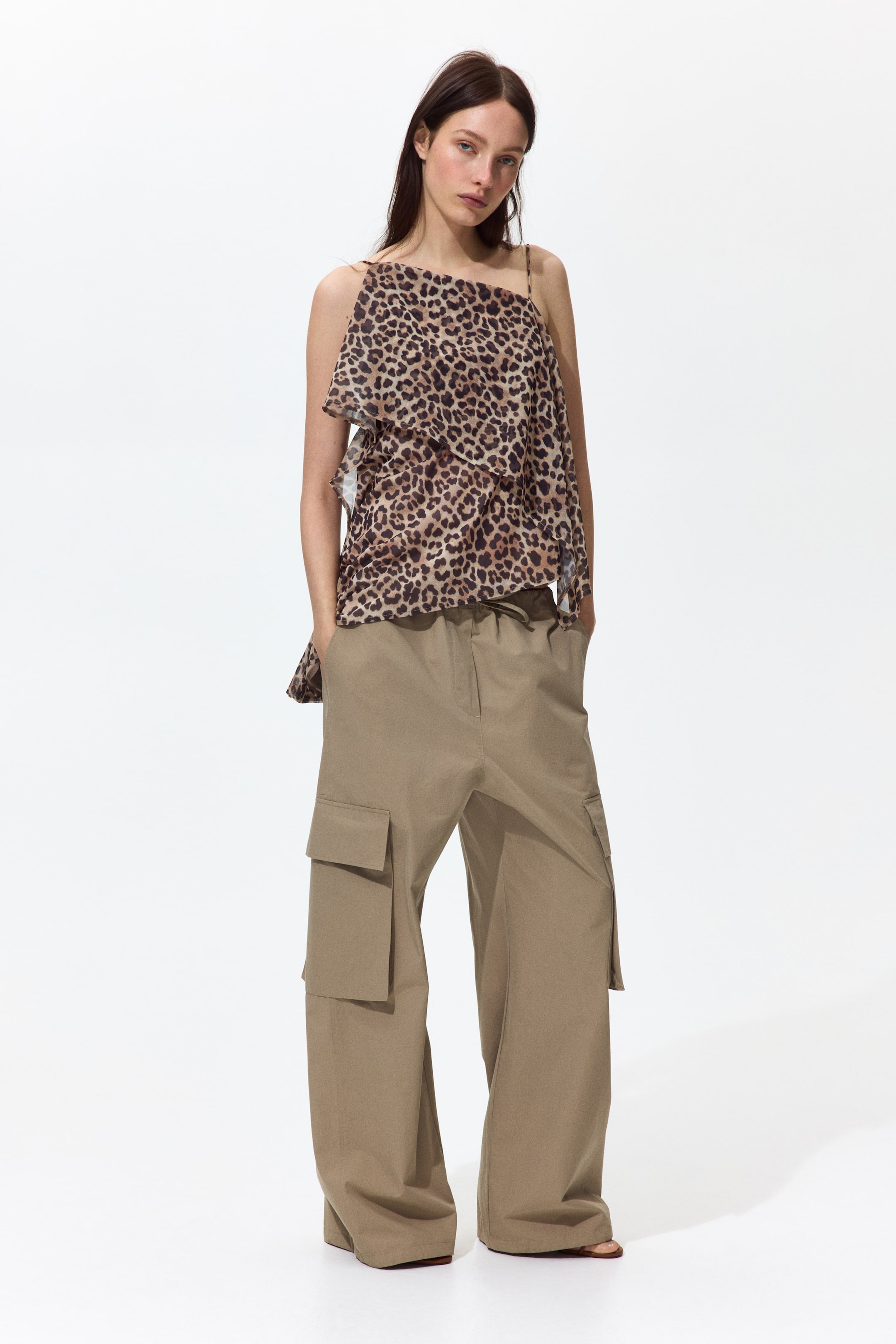 Voir une image plus grande: Un haut camisole à imprimé léopard en couches et un pantalon cargo kaki à jambes larges sont présentés comme une tenue, face à l'avant. Le camisole présente une bretelle spaghetti d'un côté et une bretelle plus large de l'autre, avec des couches à volants qui descendent en cascade, tandis que le pantalon cargo affiche de grandes poches à rabat sur les cuisses et une taille élastique à cordon de serrage.