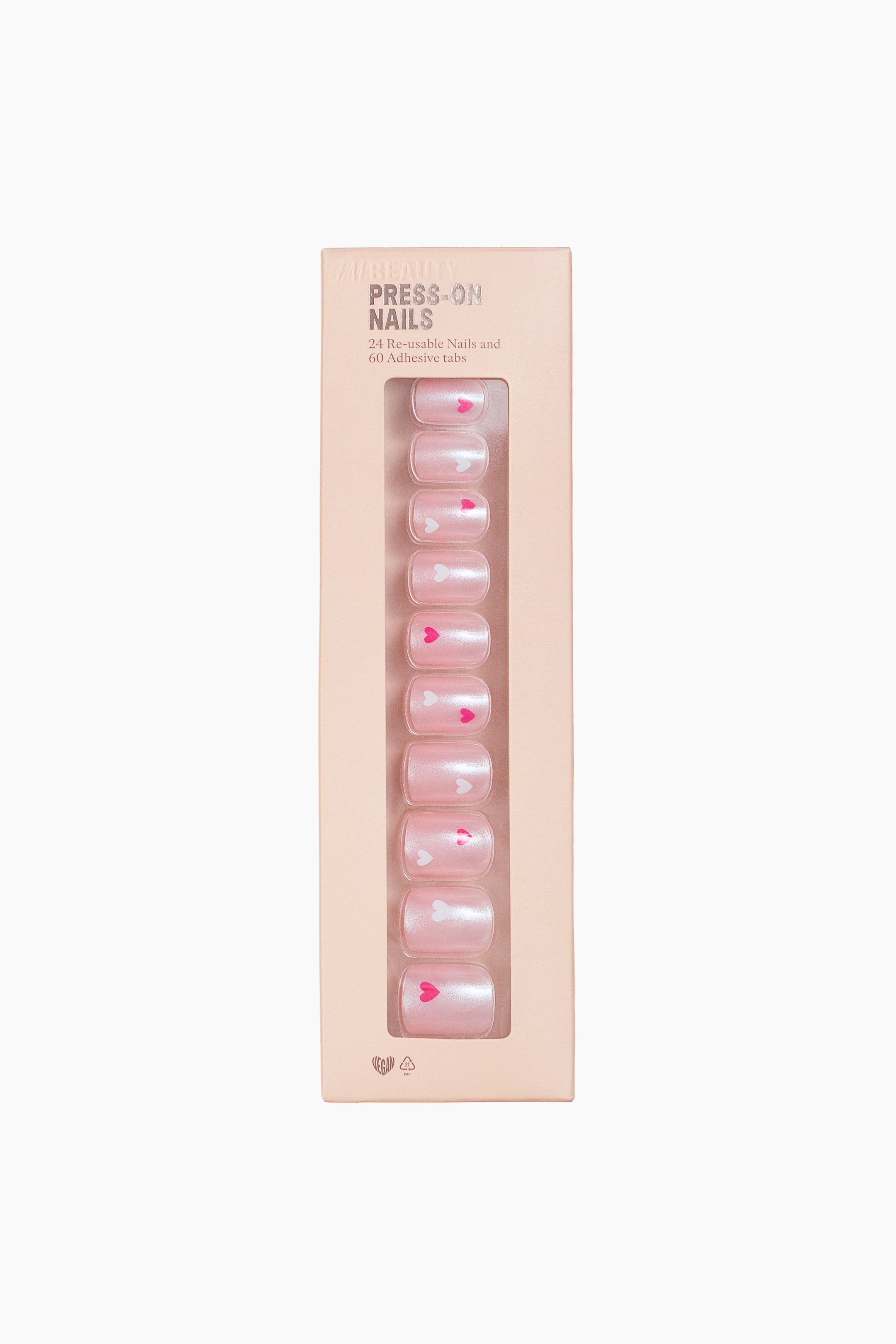 View larger image: A light peach-colored box of press-on nails is facing FRONT, displaying ten pearlescent pink nails through a clear window. Each nail is featuring alternating white and fuchsia heart designs, and the box is indicating "24 Re-usable Nails and 60 Adhesive tabs."