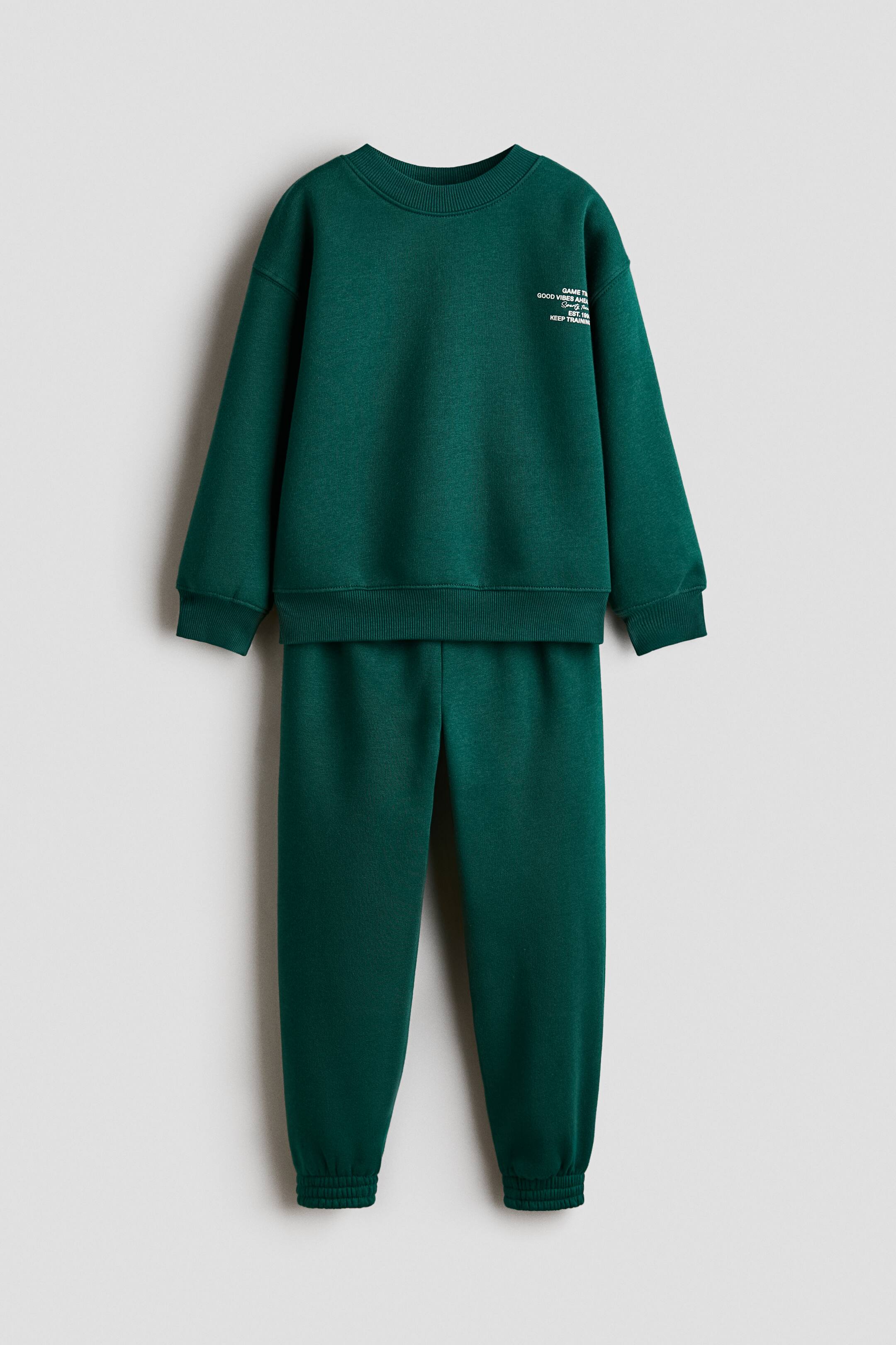 View larger image: A dark green sweatshirt and joggers set is shown from the front. The sweatshirt features a white print motif on the upper left chest, a round rib-trimmed neckline, dropped shoulders, and wide ribbed trims at the cuffs and hem, while the joggers feature an elasticated waist and elasticated hems.
