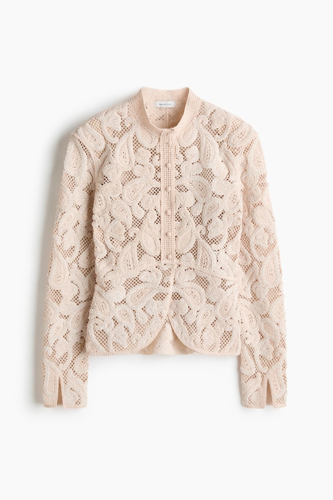 A light peach lace jacket is laid flat and facing forward, showcasing an intricate paisley-like openwork pattern throughout. It is crafted with a stand-up collar, a central button placket, and a curving bottom hem. - 1
