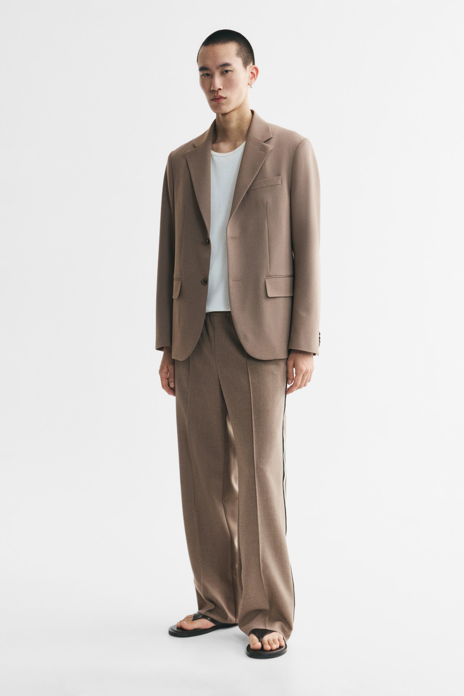 The brown trousers feature an elasticated waistband and a vertical crease running down the front of each leg. Triple stripes, consisting of black and light yellow bands, accentuate the outer seams of both trouser legs. - 1