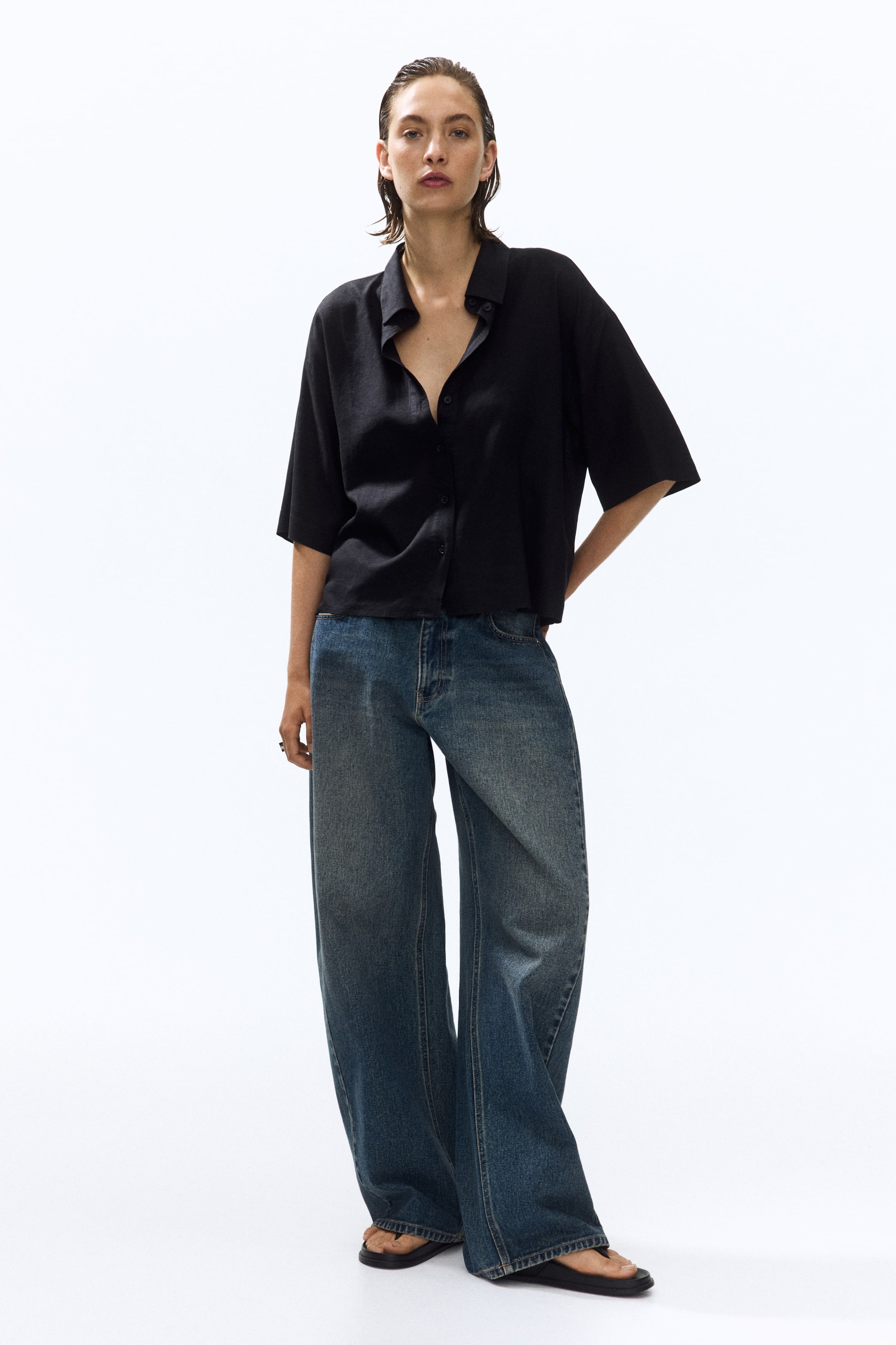 Visualizza l'immagine ingrandita: Una camicia oversize nera in un leggero misto di lino e viscosa, caratterizzata da un colletto, bottoni sul davanti, spalle scese e maniche al gomito, è indossata dalla modella e abbinata a jeans a gamba larga.