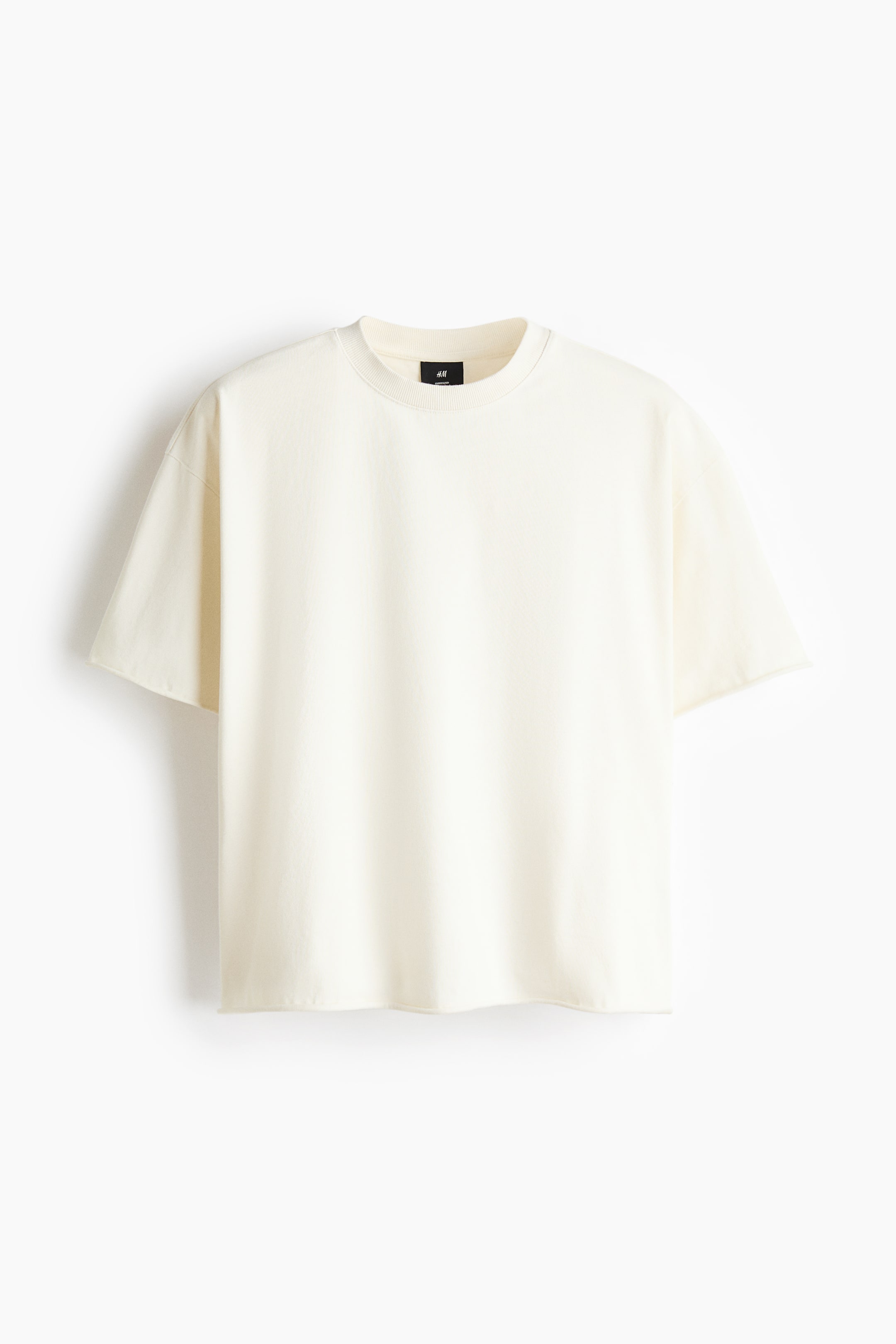 View larger image: The front of a light cream, boxy-style T-shirt is showcased. It features a round, rib-trimmed neckline, dropped shoulders, and a straight-cut hem, creating an oversized, baggy, extra-loose silhouette.