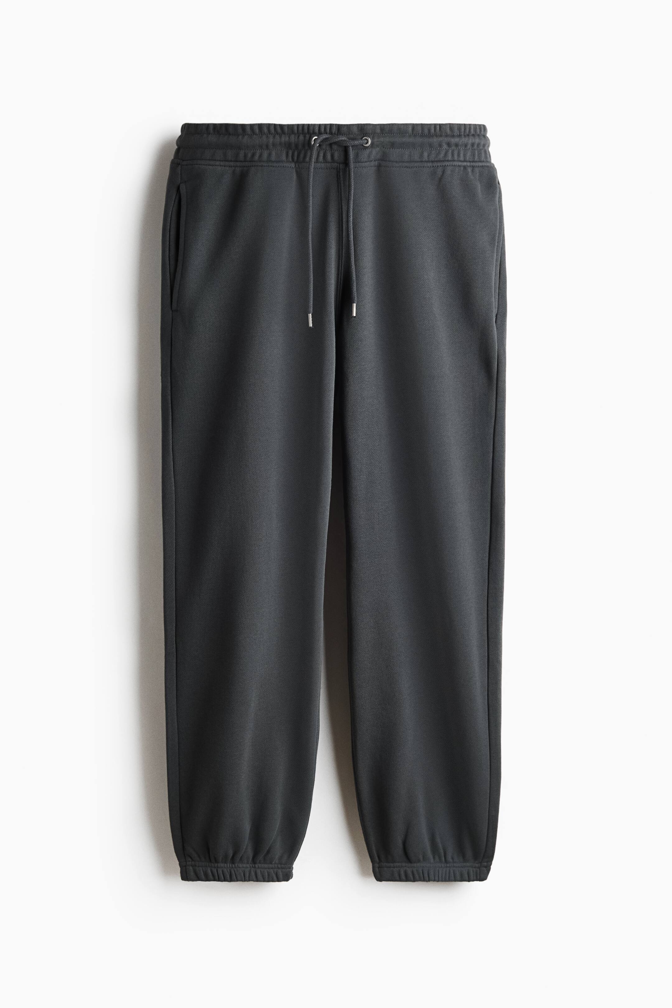 View larger image: Dark grey sweatpants are shown from the front, featuring a smooth texture, a drawstring waist with metal-tipped cords, vertical side seam pockets, and elasticated ankle hems, conveying a relaxed fit.