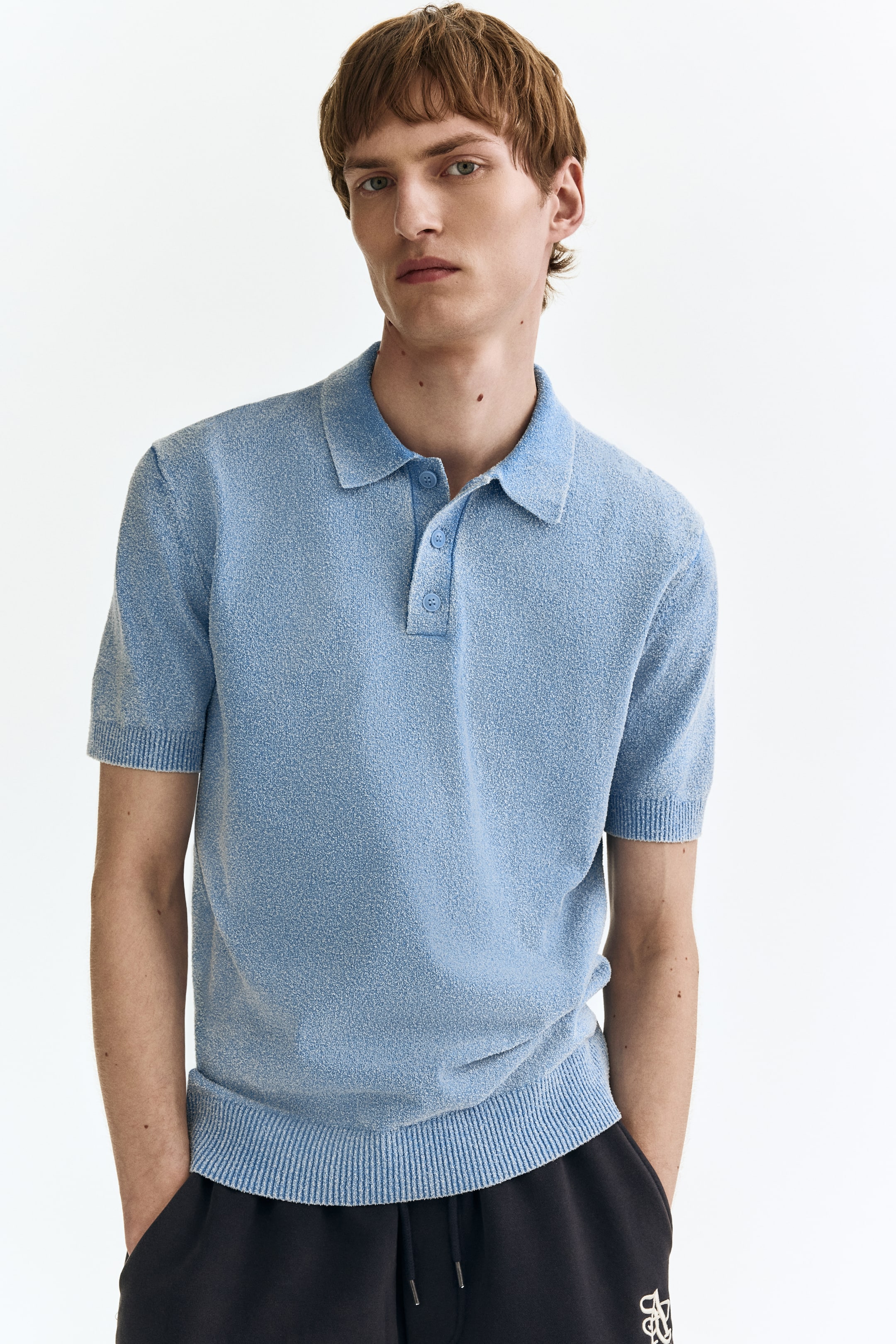 View larger image: A light blue textured knit polo shirt featuring a classic collar and a two-button placket with matching light blue buttons. Designed with short sleeves, ribbed cuffs, and a ribbed hem, it offers a relaxed fit.
