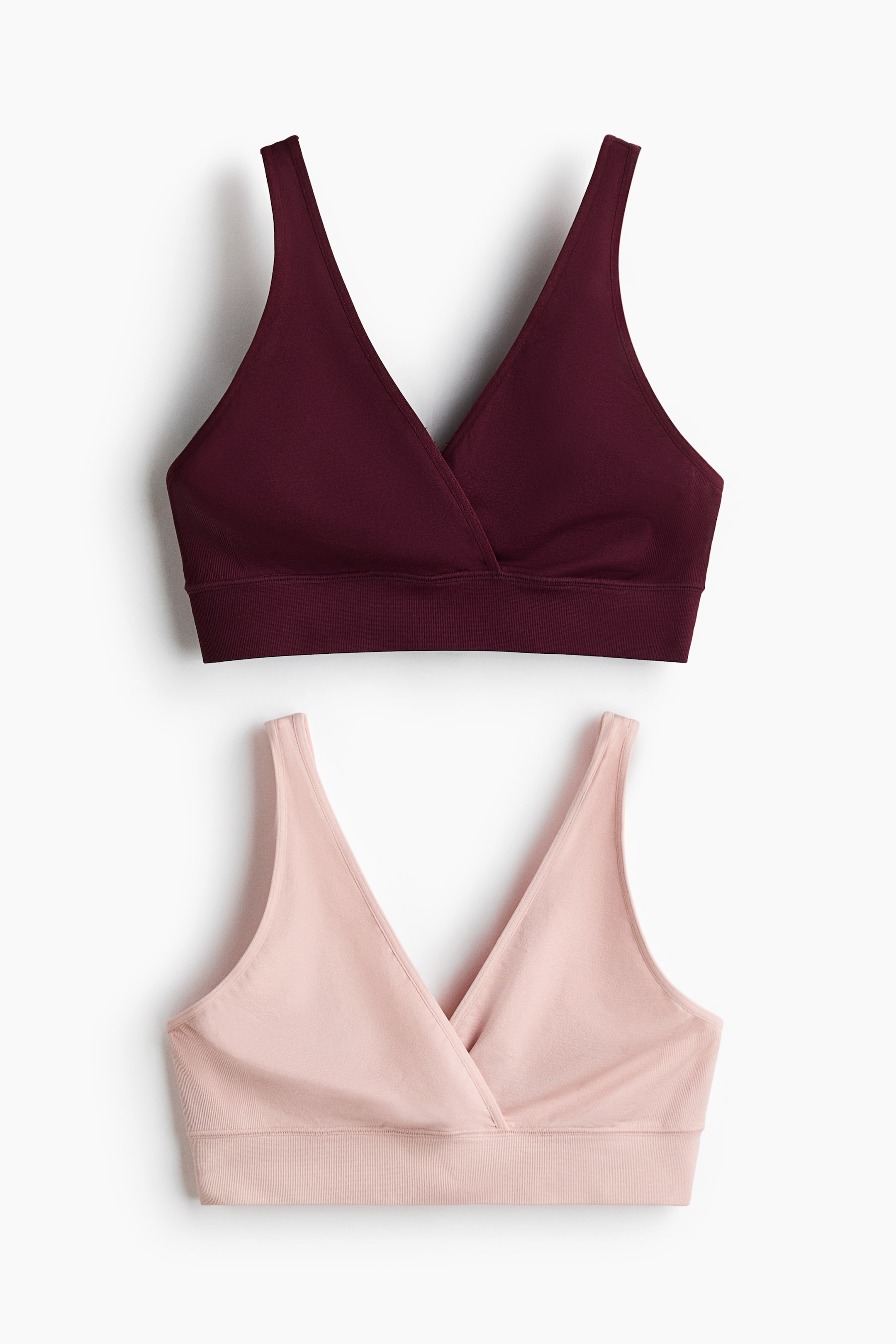 View larger image: Two non-wired nursing bras, one in a rich maroon and the other in a soft light pink, are displayed from the front. Each bra is designed with broad shoulder straps, a wrapover front for easy nursing access, and wide ribbing at the hem for added comfort.