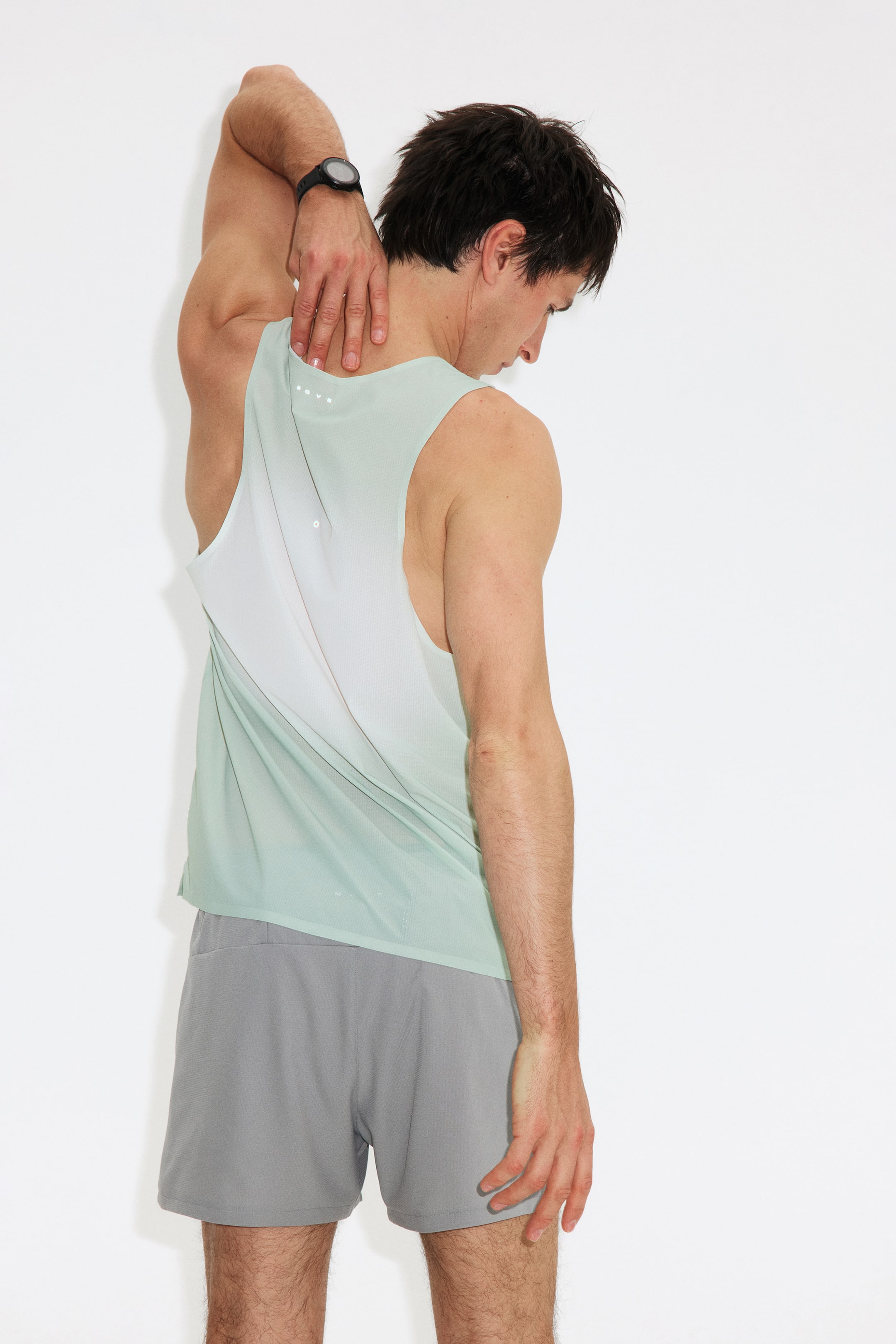 View larger image: A light green athletic tank top, viewed from a back-side angle, showcases a white panel design on the upper and mid-back, with "ROVE" printed at the neckline. It is paired with light grey athletic shorts.
