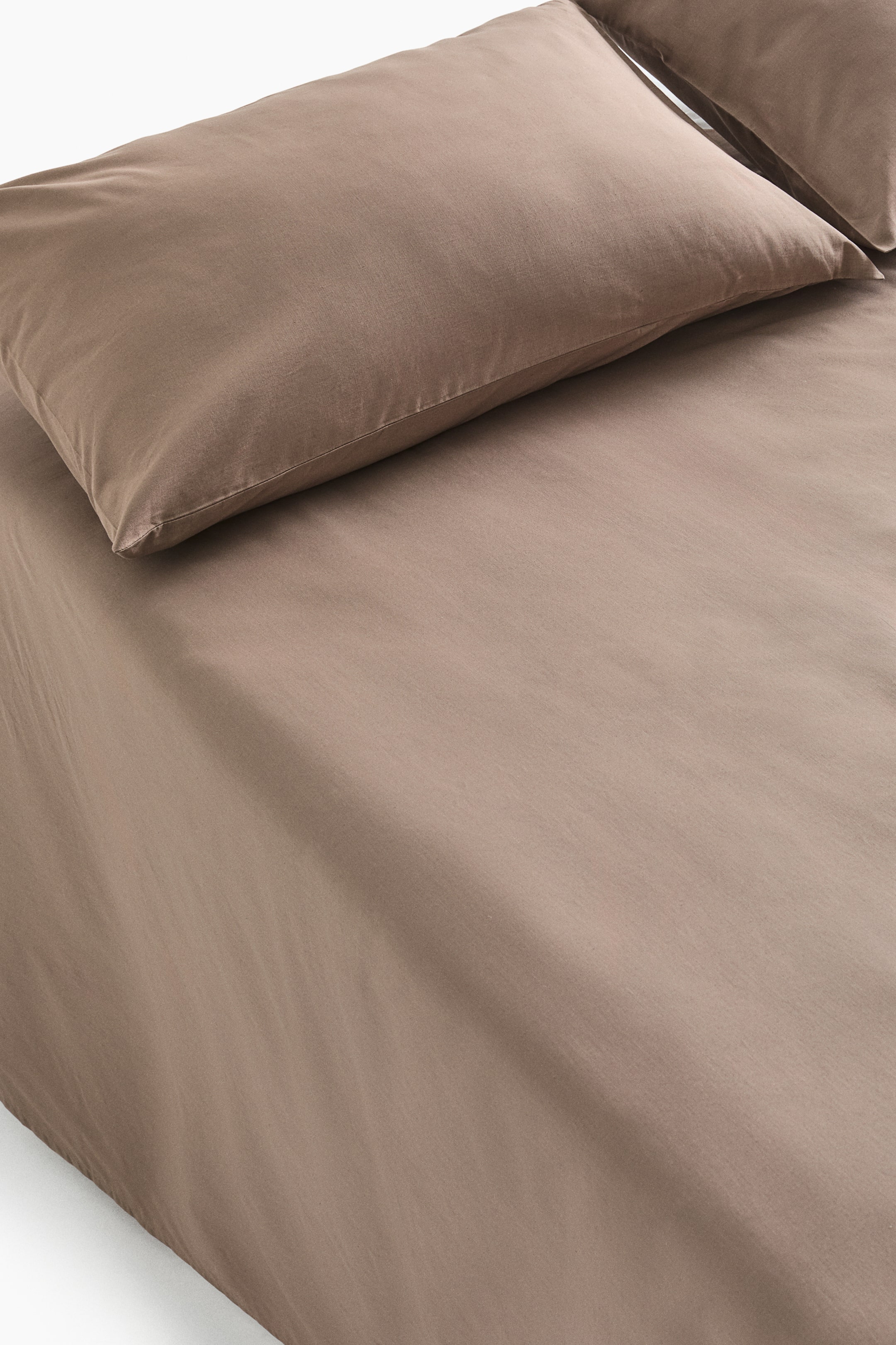 View larger image: A light brown bed sheet set is shown featuring a flat sheet and two pillowcases, one fully visible and angled towards the upper left, the other partially visible behind it. All pieces display a soft cotton weave texture, with the flat sheet extending downward.