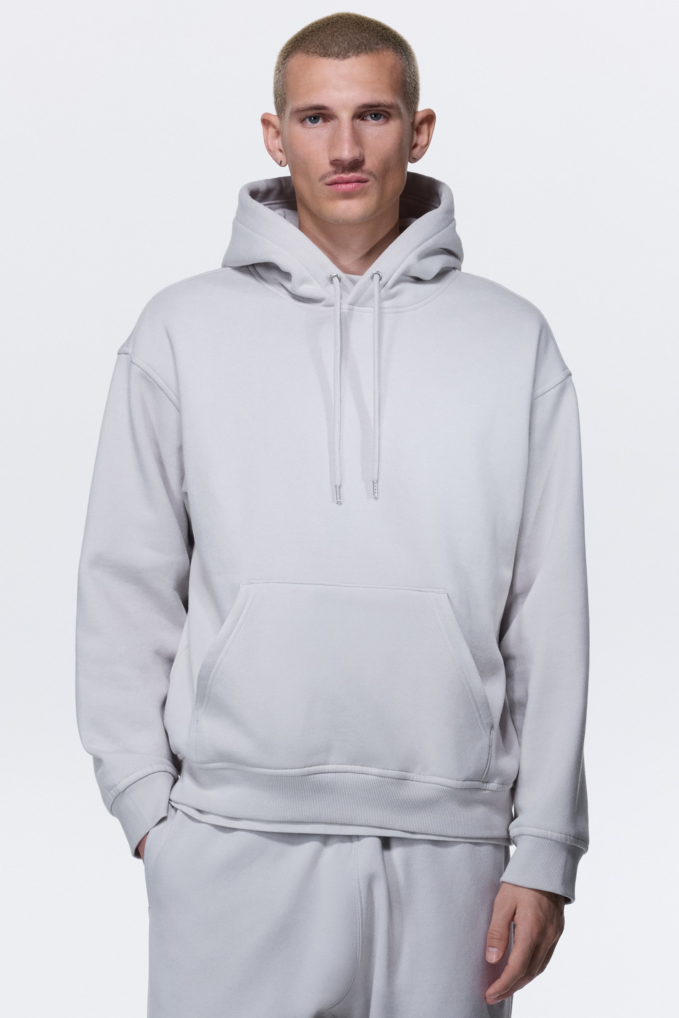 View larger image: A light gray hoodie features a drawstring hood with matching drawstrings, a front kangaroo pocket, and ribbed cuffs and hem, offering a relaxed fit.