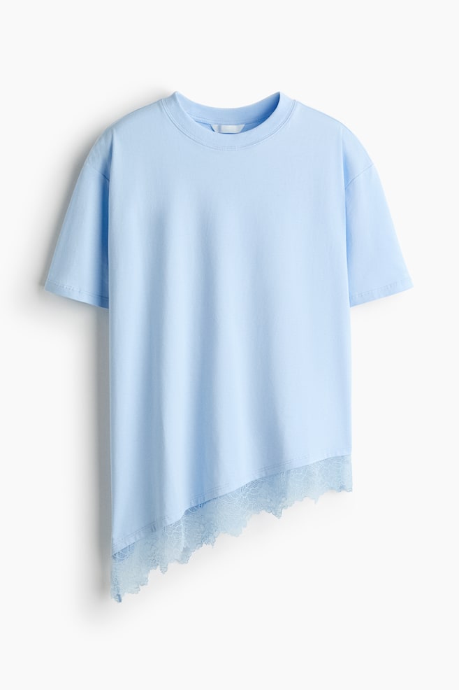 A light blue relaxed-fit T-shirt is hanging front-facing, featuring a ribbed crew neck, dropped shoulders, and short sleeves. The T-shirt showcases an asymmetrical hem that slopes downward, finished with a matching light blue scalloped lace trim. - 1