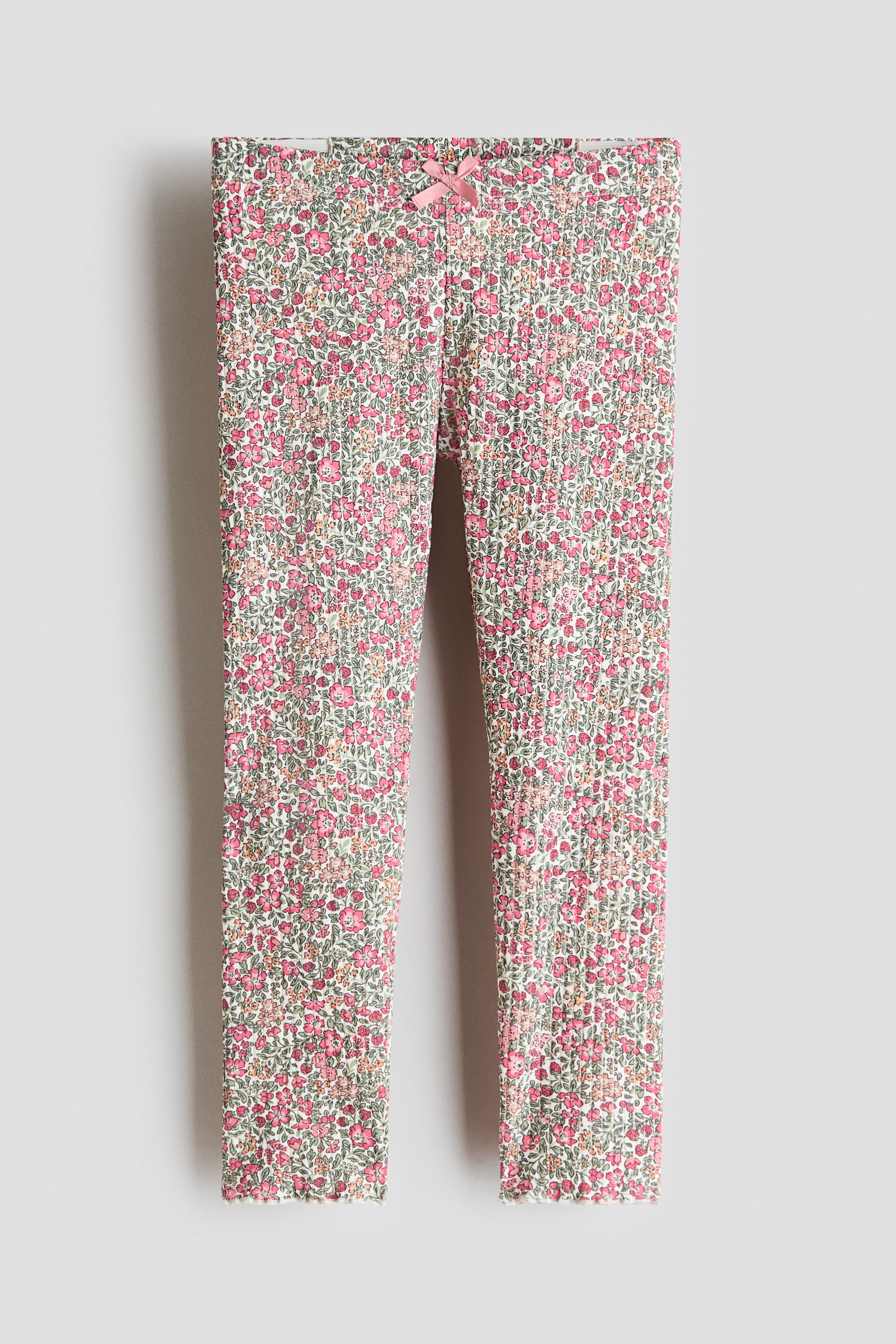 View larger image: Leggings showcase a delicate floral pattern throughout, featuring shades of pink, green, and light yellow on a ribbed jersey texture. A dainty pink satin bow embellishes the center of the waistband, while the leg openings boast a subtle wavy finish.