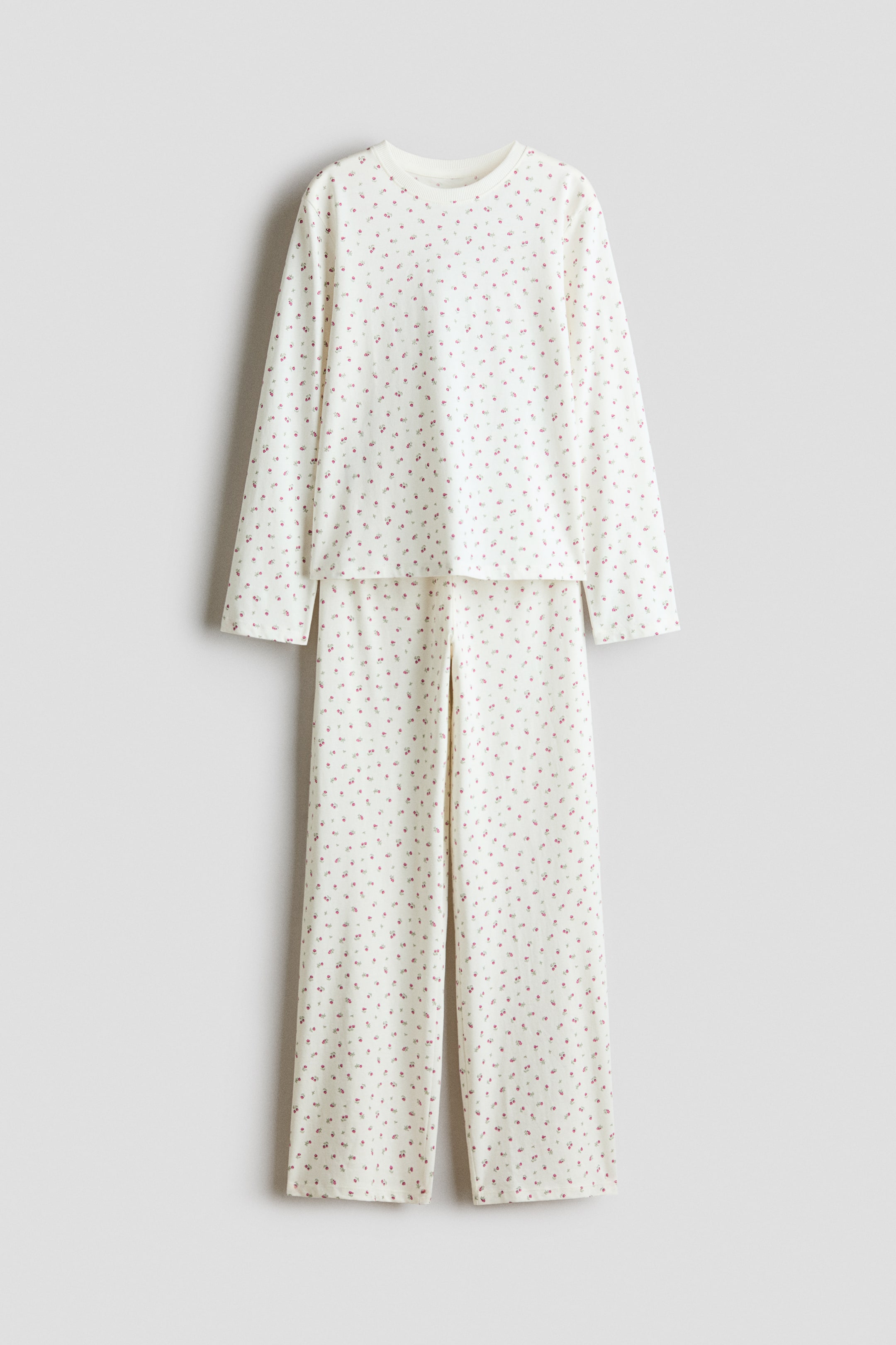 Größeres Bild anzeigen: Ein zweiteiliges Pyjama-Set ist von vorne zu sehen, bestehend aus einem Langarmshirt und einer passenden gerade geschnittenen Hose aus cremeweißem Stoff mit einem durchgehenden Kirschen-Print in Rosa und Rot. Das Shirt zeigt einen runden, mit Rippbündchen eingefassten Ausschnitt, während die Hose gerade fällt und den lässigen Schnitt zur Geltung bringt.