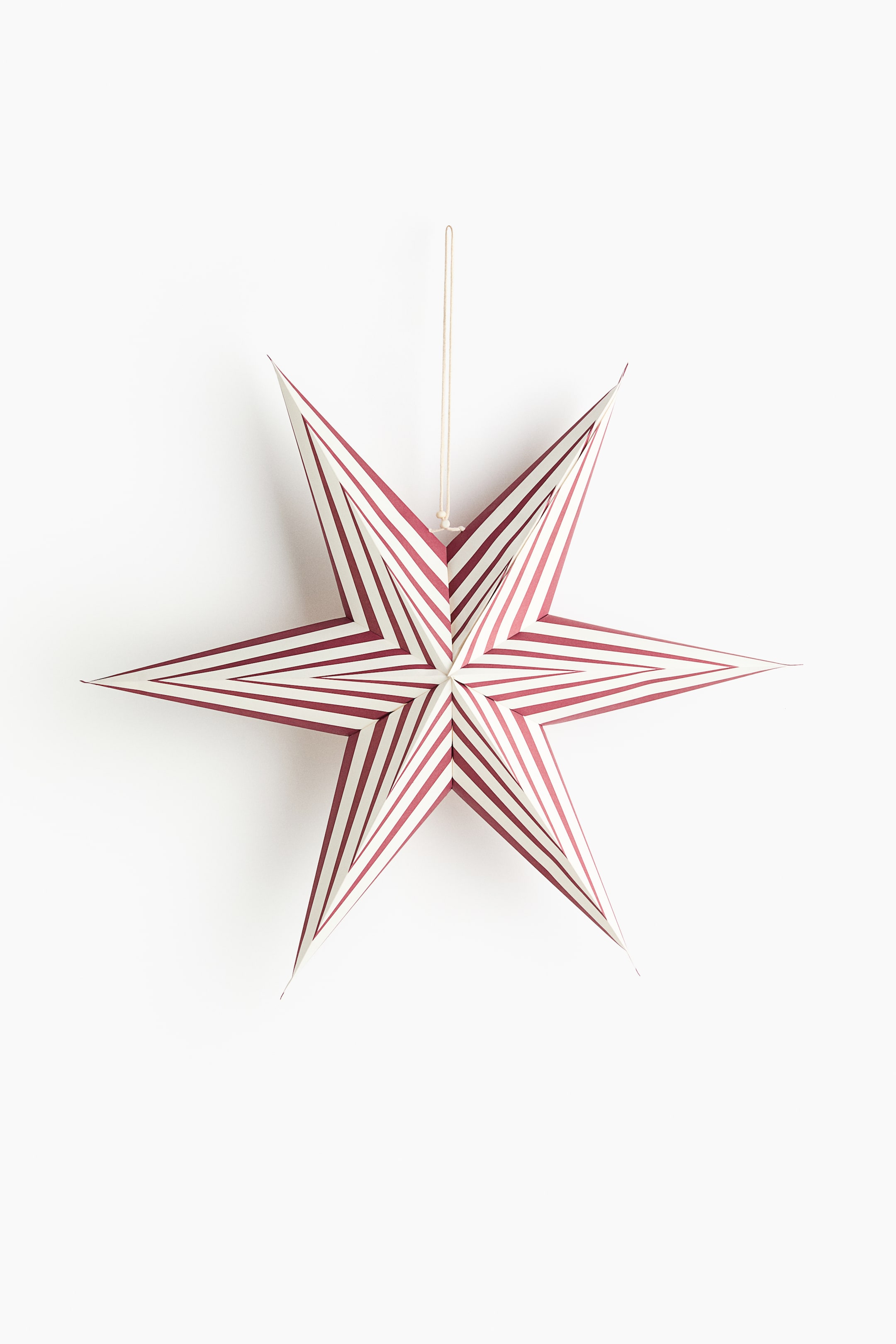 Näytä suurempi kuva: Kuusipisteinen, kolmiulotteinen paperitähtikoriste roikkuu, edessä. Se esittelee punaisten ja valkoisten raitojen kuvion, joka hahmottelee sisäkkäisiä tähtimuotoja, ja sen yläosassa on kiinnitetty vaaleanvärinen naru ripustamista varten.