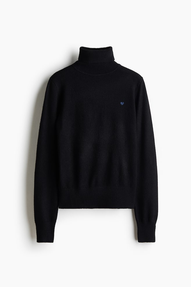 Ein schwarzer Strickpullover ist von vorne zu sehen, mit geripptem Rollkragen, langen Ãrmeln mit gerippten BÃ¼ndchen und geripptem Saum. Ein kleines, blaues, gesticktes Herz ziert die linke Brust des weich gestrickten KleidungsstÃ¼cks. - 1