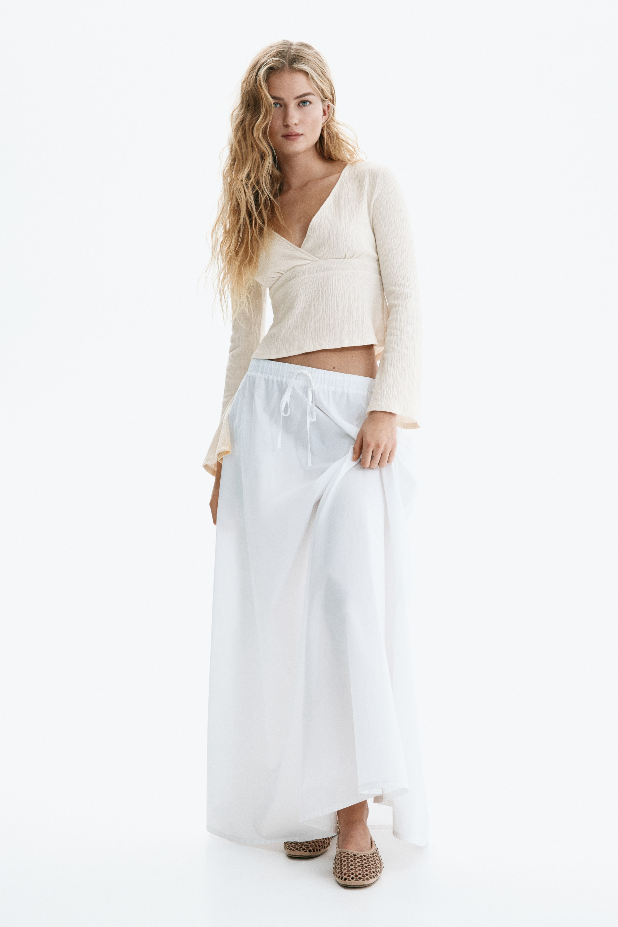 View larger image: A cream textured wrap-style crop top features a V-neckline and long, flared sleeves, shown front-facing. It is paired with loose-fitting white wide-leg pants displaying a visible drawstring waist and a relaxed, full-length silhouette.
