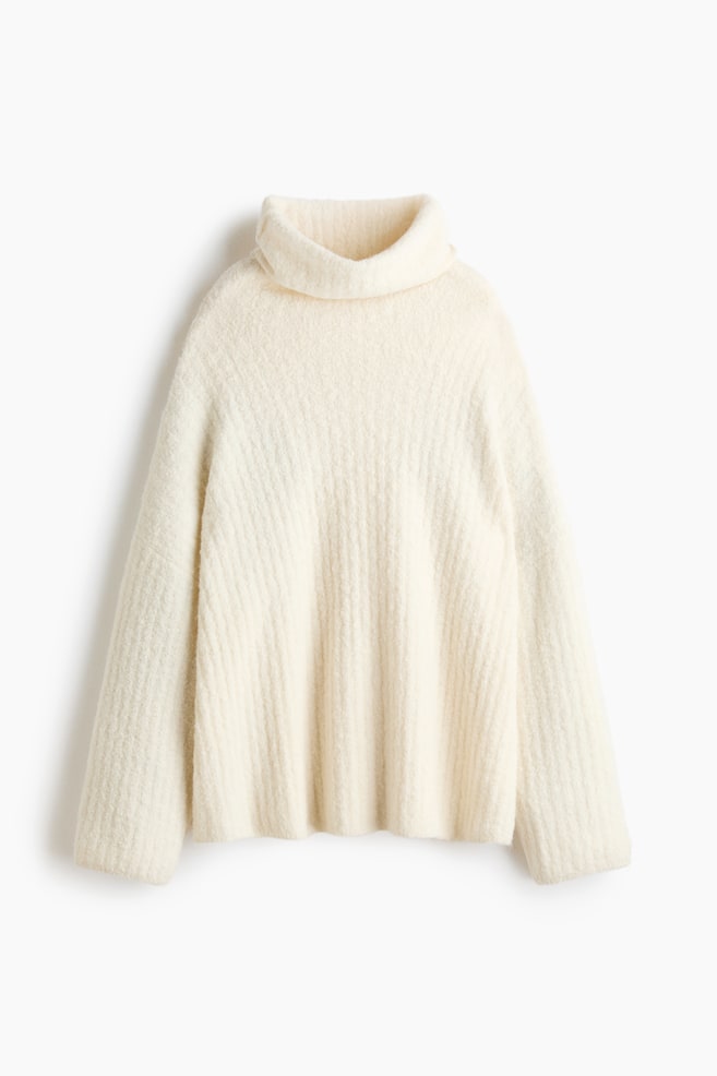 An off-white knitted sweater is shown from the front, featuring a loose roll-neck collar and a textured ribbed design throughout. The sweater has a relaxed, oversized fit with dropped shoulders and long, wide sleeves. - 1