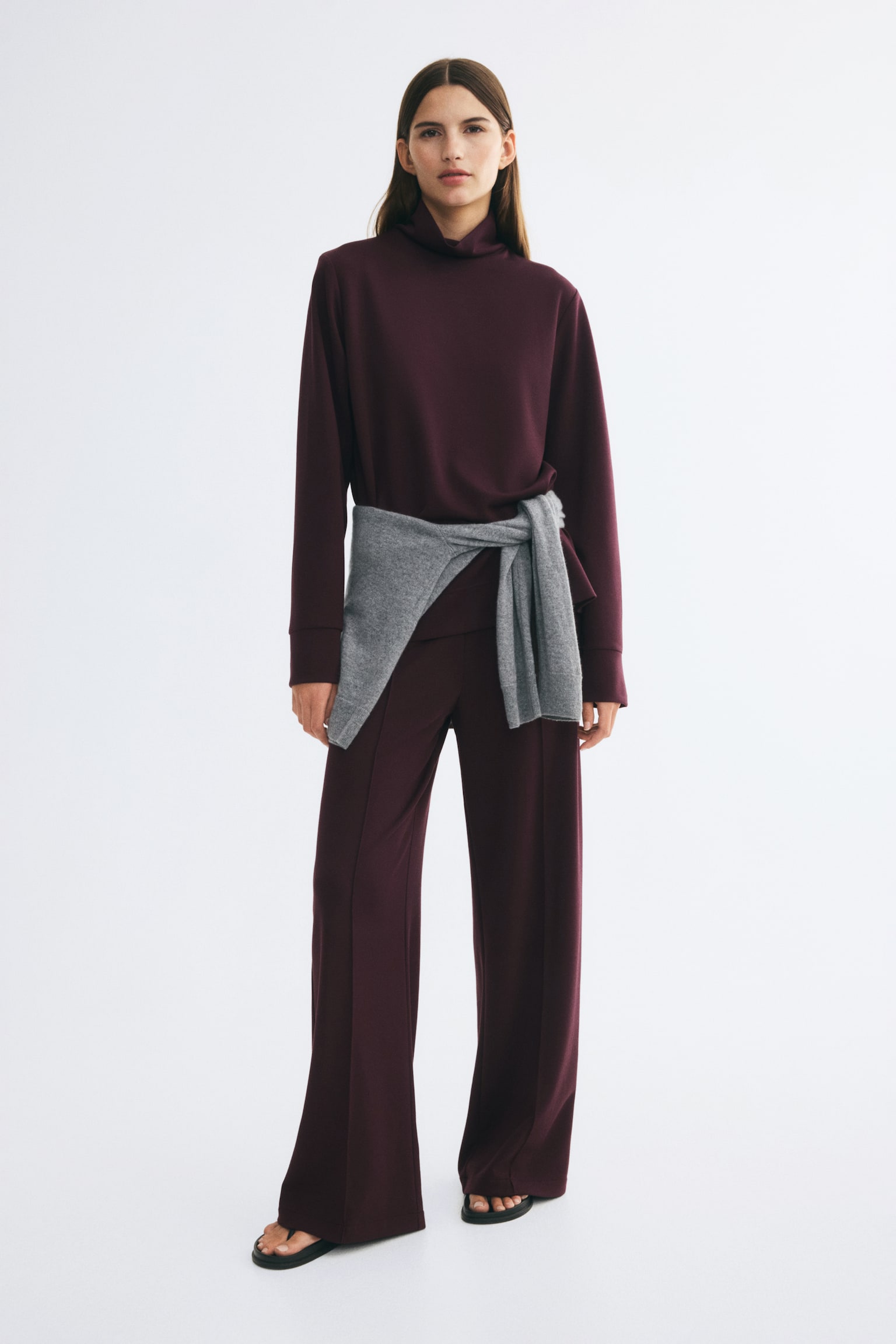 A dark plum jersey set is shown from the front, featuring a long-sleeved top with a stand collar and wide cuffs layered over matching straight-leg trousers. The trousers feature prominent sewn-in creases running down the centre of each leg. - 1