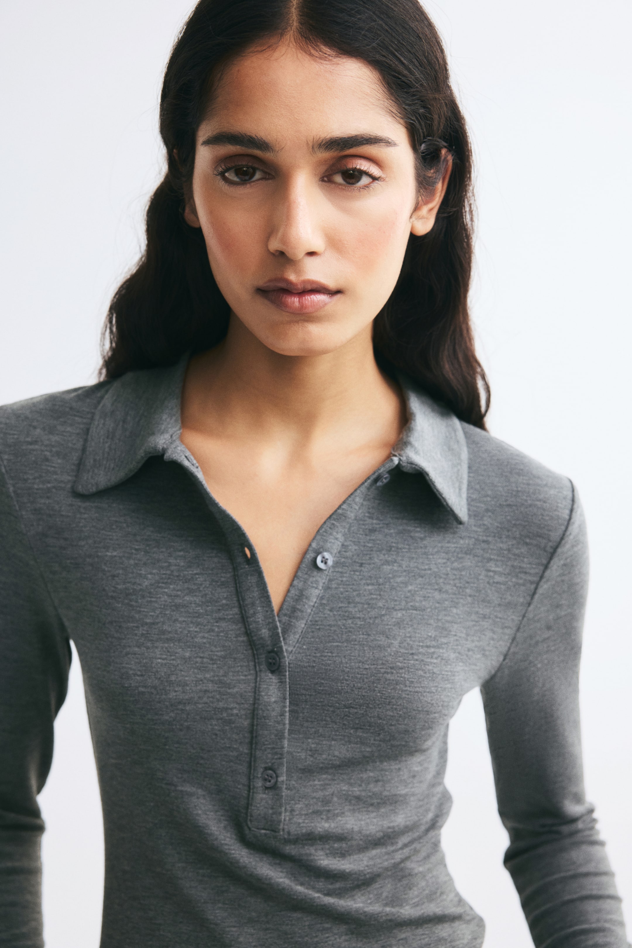 View larger image: A grey, fitted polo shirt in stretch jersey is shown from the front, featuring a classic collar, a button placket, and long sleeves. The lightweight fabric sits close to the body to highlight the shirt's slim fit.