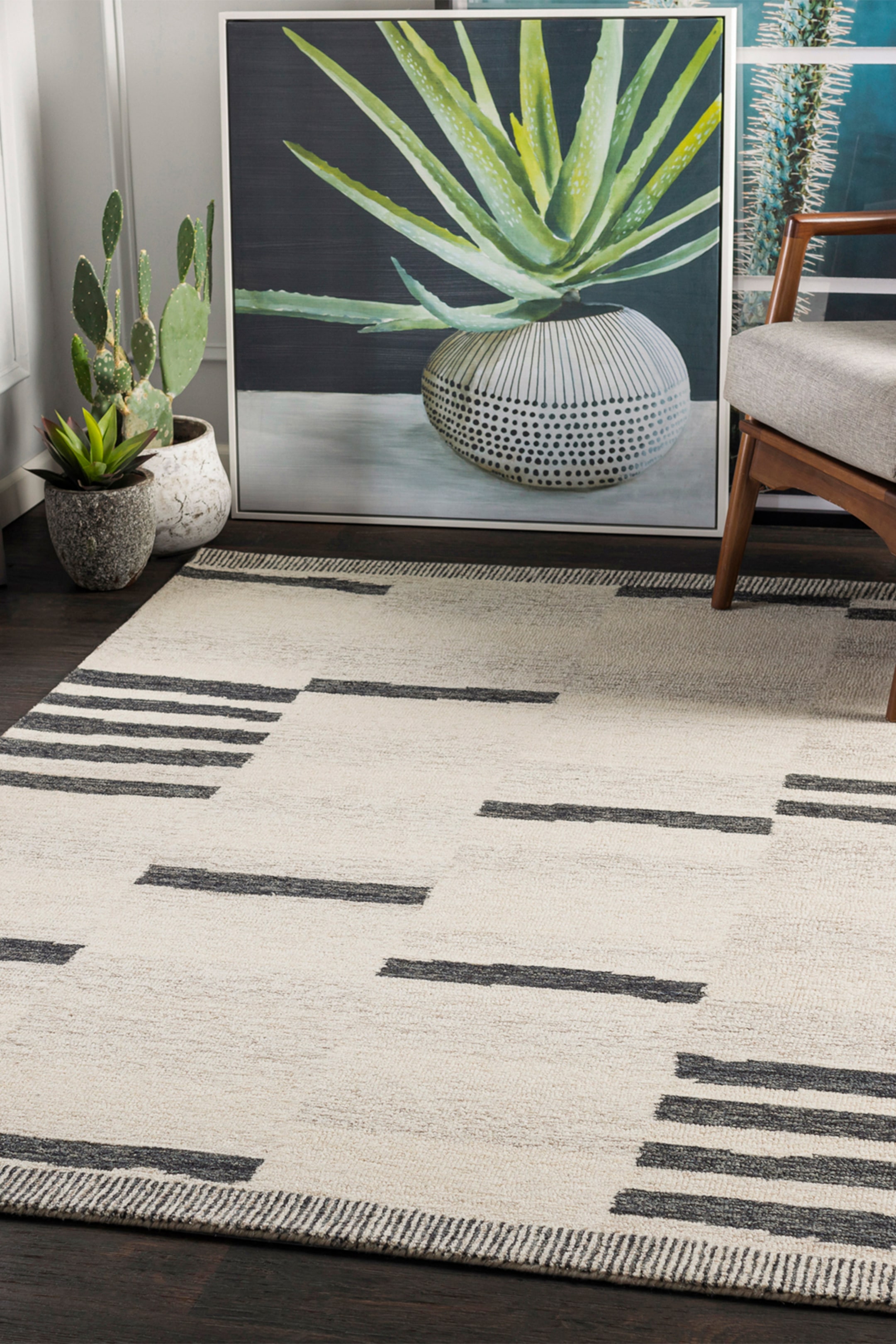View larger image: An area rug is showcasing a modern geometric pattern with a cream-coloured textured pile and scattered blocks of dark charcoal horizontal stripes of varying lengths and thicknesses. The top and bottom edges feature a thin, densely striped border.