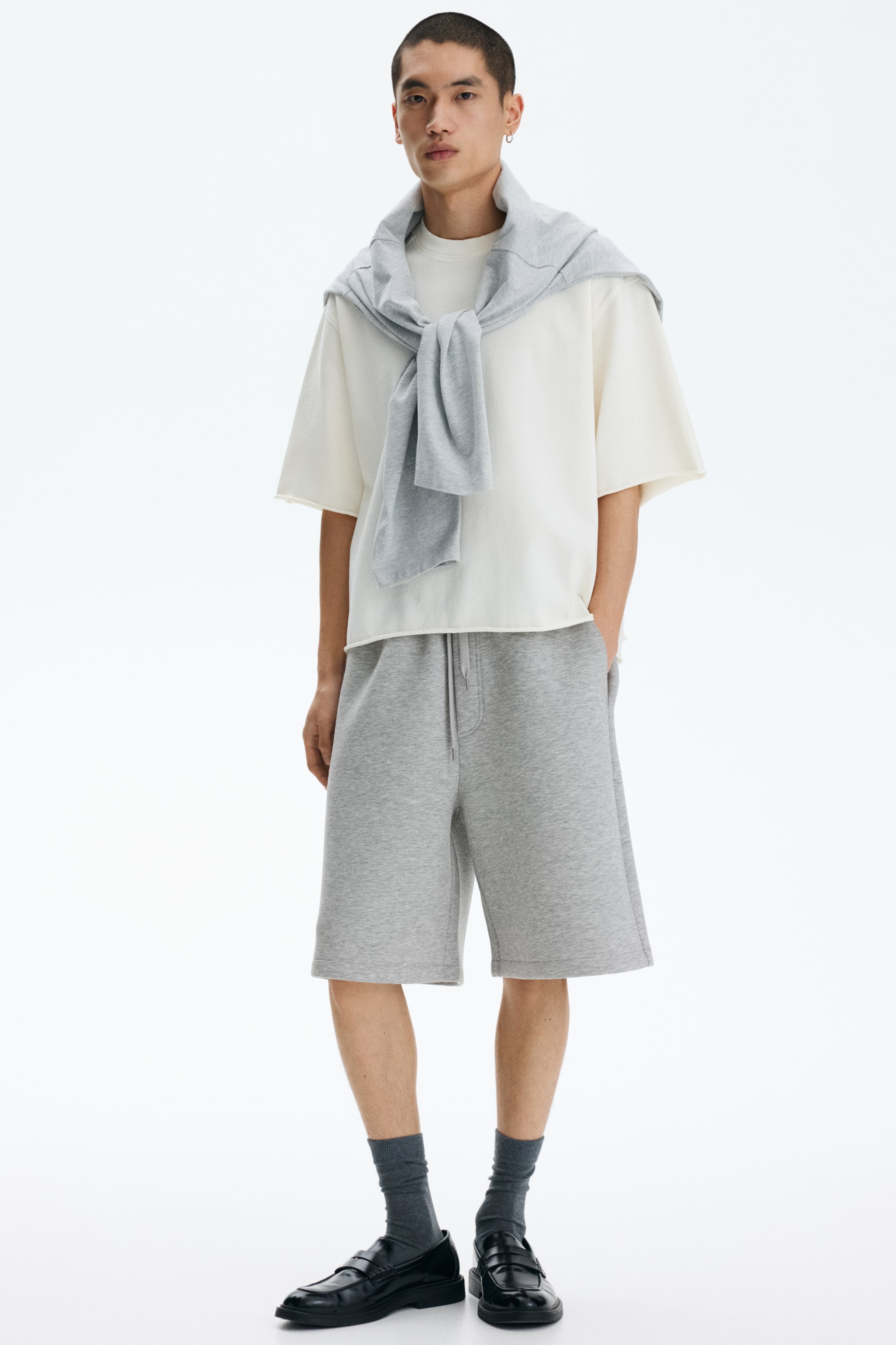 Voir une image plus grande: Les shorts de jogging gris offrent une coupe décontractée, avec une taille élastiquée dotée d'un cordon de serrage visible, et s'étendent juste au-dessus des genoux.