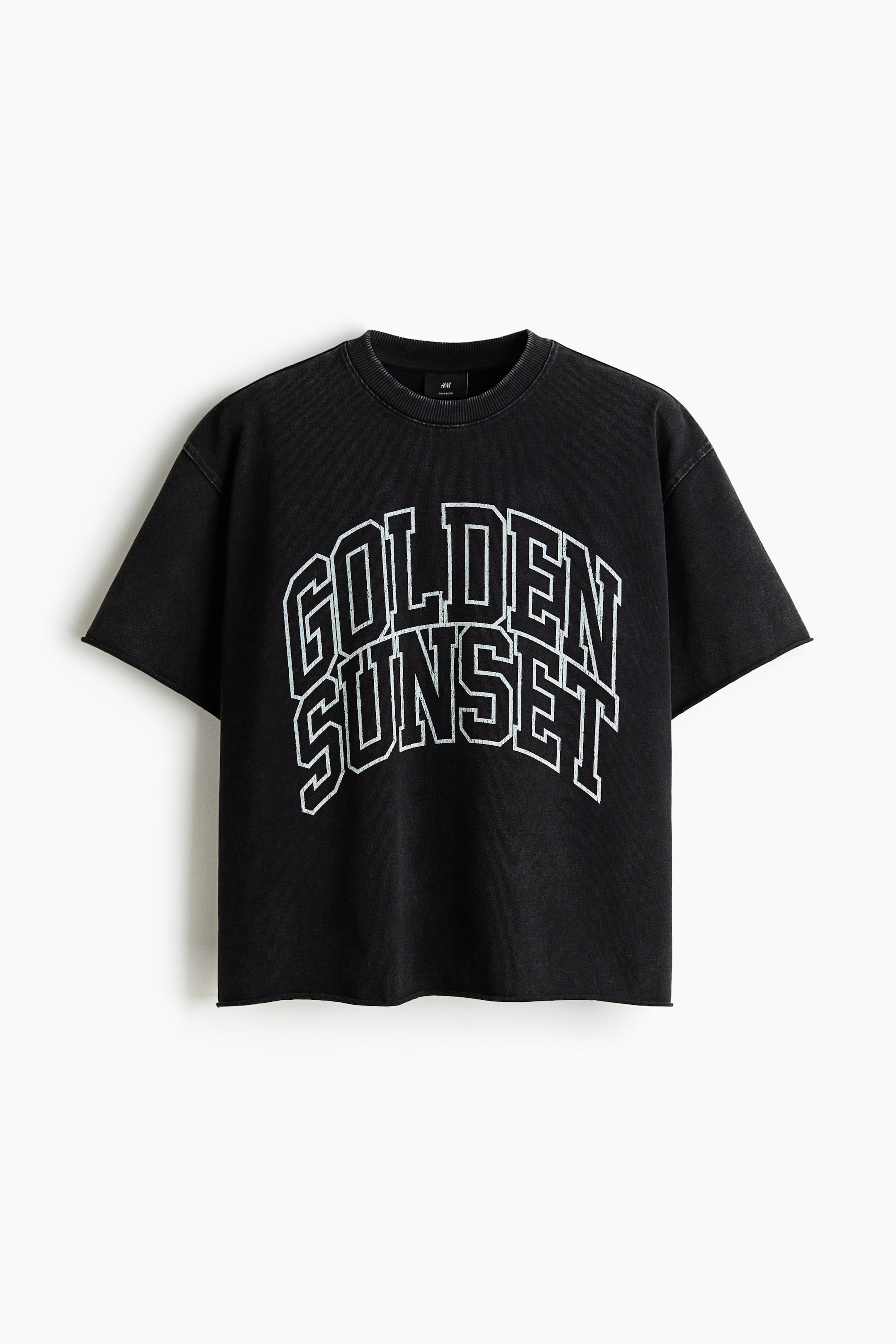 Se større billede: En bokseformet T-shirt i en udvasket sort nuance har en oversized og løs pasform med lavtsiddende skuldre og kortærmer med rå kant. FRONTEN viser en buet 'GOLDEN SUNSET' grafik i forrevet hvid konturtekst sammen med en rund halsudskæring med ribkanter og en lige rå skåret kant.