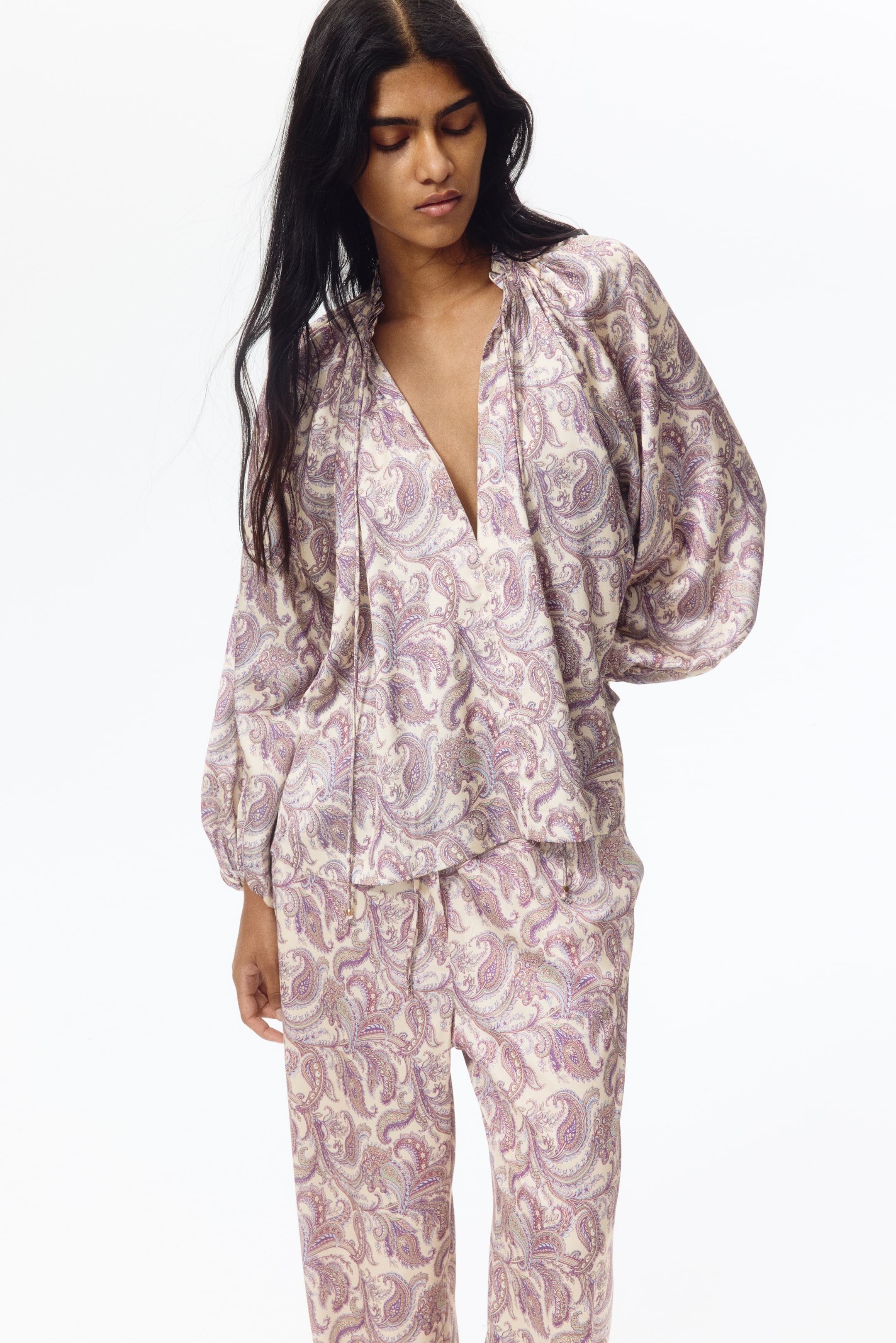View larger image: A matching cream paisley print top and pants set is displayed from a slight front angle. The top showcases a V-neckline with drawstring ties, gathered detailing around the neck, and long sleeves with elasticized cuffs, while the coordinating pants feature side pockets and a relaxed fit.