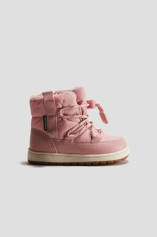 Ein rosa Winterstiefel ist in Seitenansicht nach rechts ausgerichtet und prÃ¤sentiert ein gestepptes Textil-Obermaterial sowie einen synthetischen Leder-Mudguard rund um den unteren Bereich. Er verfÃ¼gt Ã¼ber kreuzweise gefÃ¼hrte KordelschnÃ¼rsenkel mit Kordelstopper, ein flauschiges Kunstfellfutter, das am Schaftkragen sichtbar ist, sowie eine dicke cremefarbene Zwischensohle mit strukturierter GummiauÃensohle. - 1