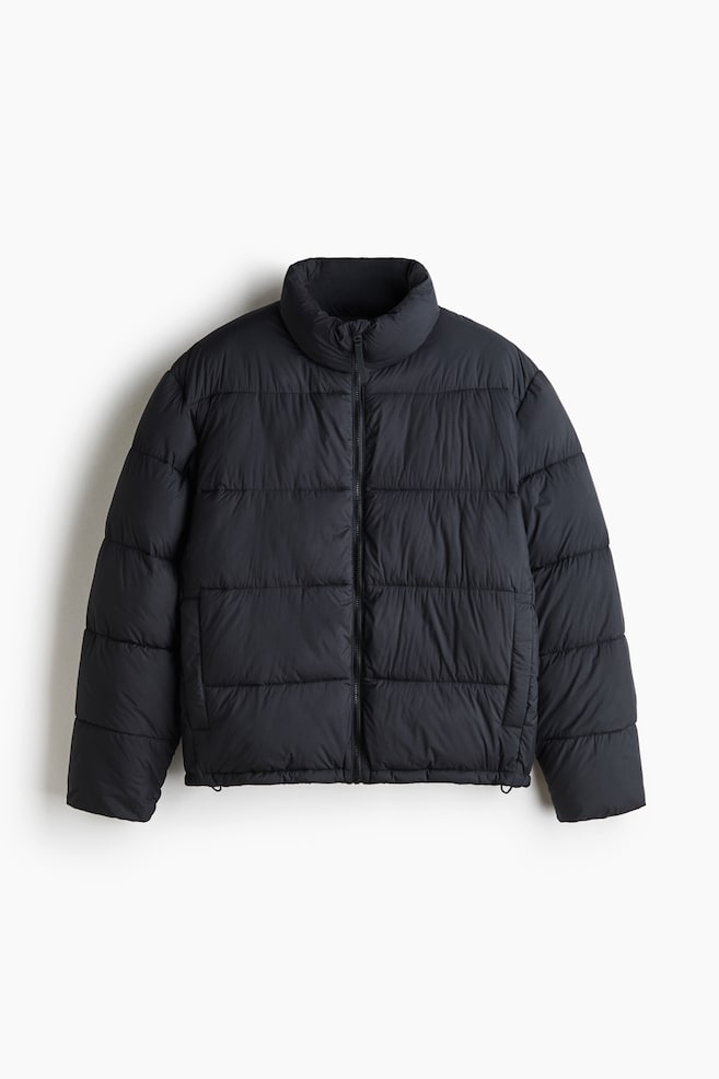 Eine schwarze, gepolsterte Pufferjacke ist frontal zu sehen und verfÃ¼gt Ã¼ber ein gestepptes Design mit horizontalen Steppkammern sowie einen hohen Stehkragen. Dargestellt sind ein durchgehender FrontreiÃverschluss, lange Ãrmel, seitliche Leistentaschen und ein verstellbarer Saum mit kleinen Kordelstoppern. - 1