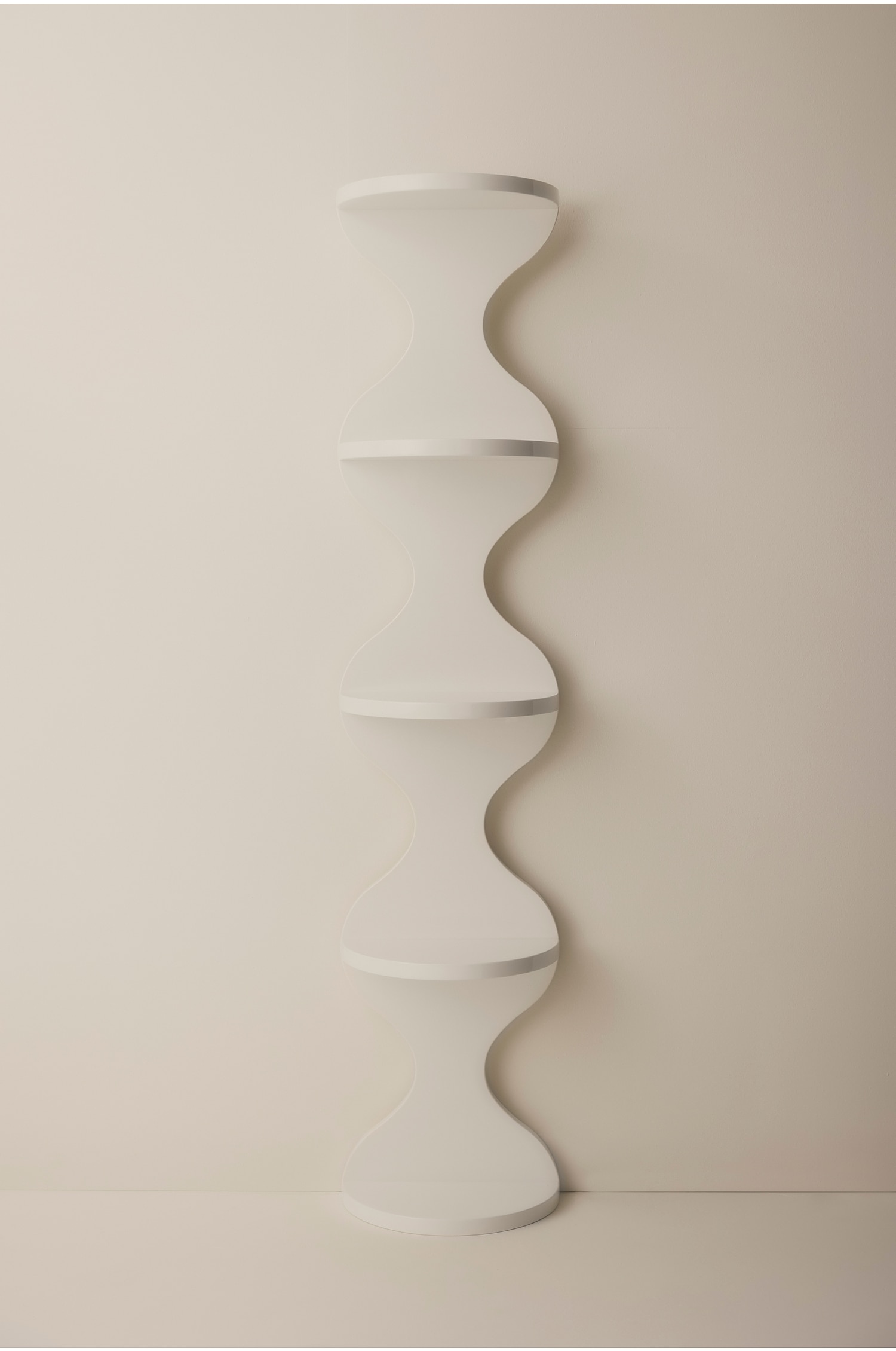 Een hoge, lichtbeige sculpturale stellingkast staat rechtop en toont een golvende, zandlopervormige silhouet met vier gestapelde, bolvormige niveaus. Elk niveau bevat een vlakke, horizontale plank, waardoor een doorlopend, golvend profiel ontstaat met een gladde afwerking.