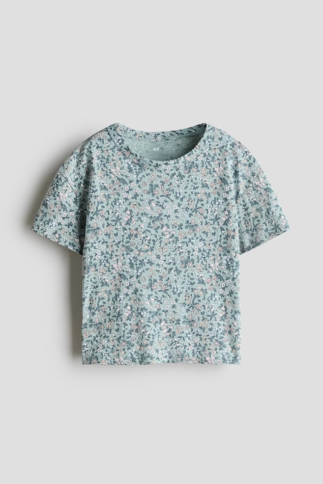 A front-facing t-shirt in light green cotton jersey is displaying an all-over pattern of small white and pink flowers. The tee is featuring a ribbed round neckline, dropped shoulders, and short sleeves. - 1