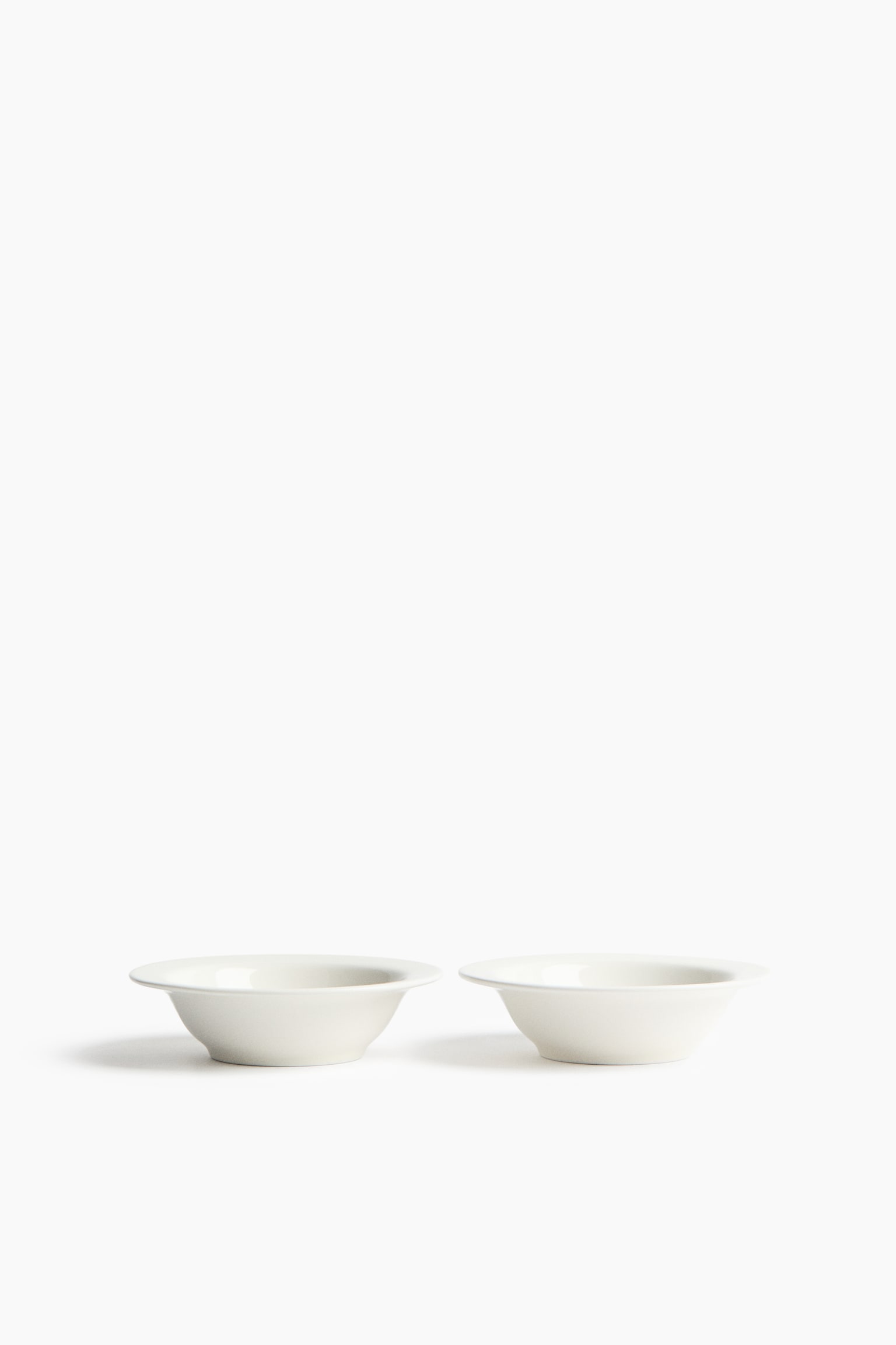 Two off-white, round ceramic bowls are sitting side-by-side, each featuring a wide, flat rim and a shallow interior. - 1