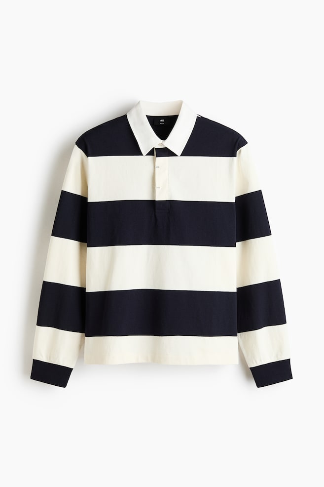 This rugby shirt is showcased from the front, highlighting its striking horizontal stripes in navy blue and off-white. It comes with a white turn-down twill collar, a hidden three-button placket, dropped shoulders, long sleeves, and ribbed cuffs. - 1