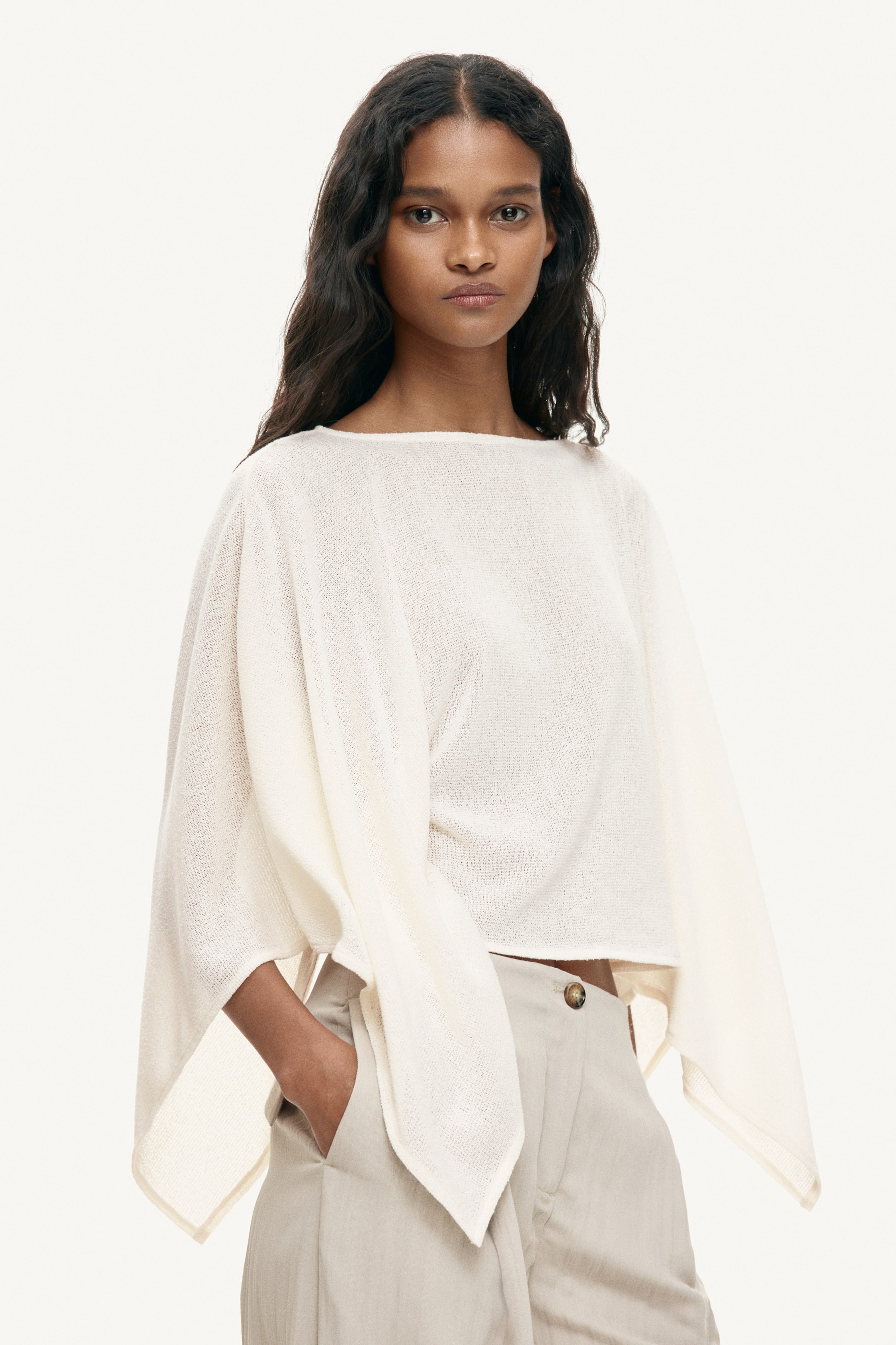 Agrandir l'image: Un haut en tricot léger de couleur blanc cassé présente un large col bateau et des manches dolman volumineuses et fluides. Il est doté d'une longueur raccourcie et d'une coupe décontractée, avec le vêtement légèrement incliné vers la droite.