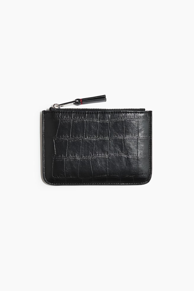 A black rectangular pouch featuring a croc-embossed texture is lying flat in a front-facing view. It is showcasing a top zipper closure with a silver-tone metal pull and a black leather pull tab accented by a small red stitch. - 1