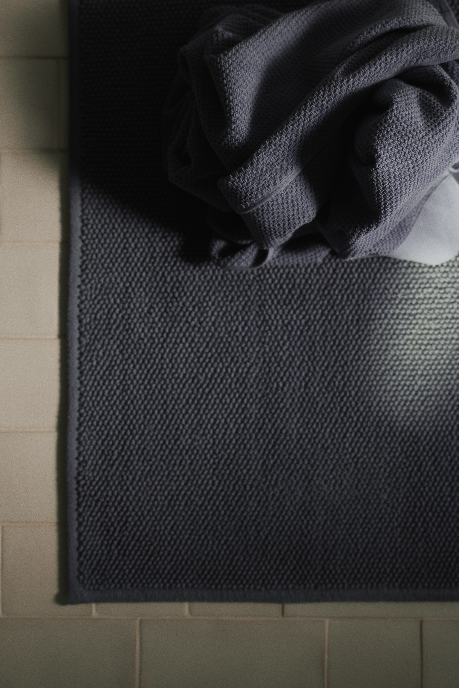 A rectangular blue-grey bath mat showcases its textured surface, featuring small, dense loops. The mat is finished with a flat, woven border along its edges. - 1