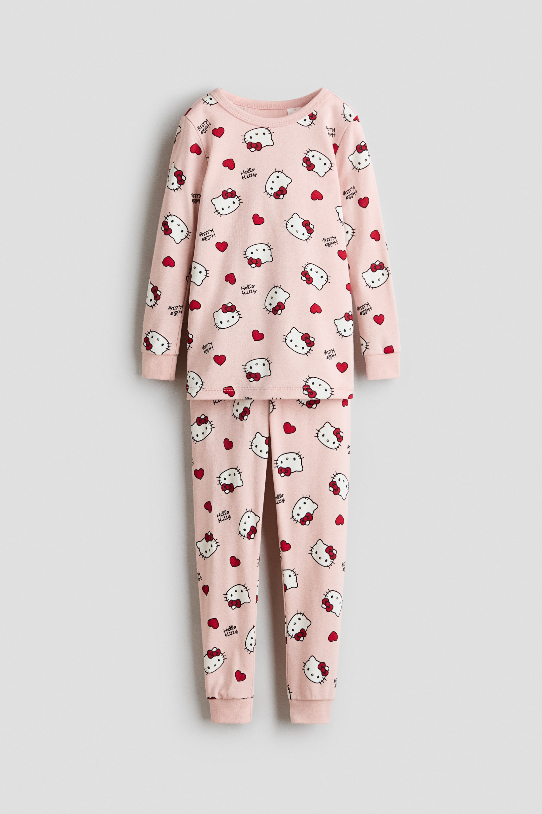 Voir une image plus grande: Un ensemble de pyjama rose deux pièces présente un motif répétitif de visages blancs de Hello Kitty avec des nœuds rouges, des cœurs rouges et le texte "Hello Kitty". Le haut à manches longues est doté d'un col rond et de poignets côtelés, tandis que le pantalon long assorti présente également des poignets côtelés aux chevilles.