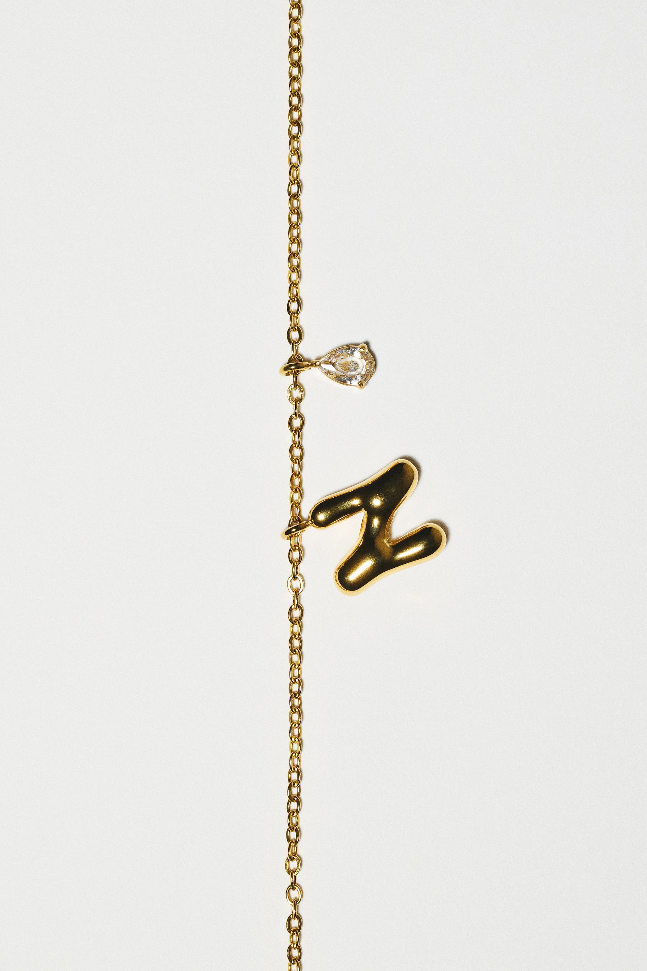 View larger image: A gold-toned stainless steel chain necklace is displaying a puffed, bubble-style letter "Z" pendant and a small, teardrop-shaped clear glass rhinestone pendant, shown from the front.