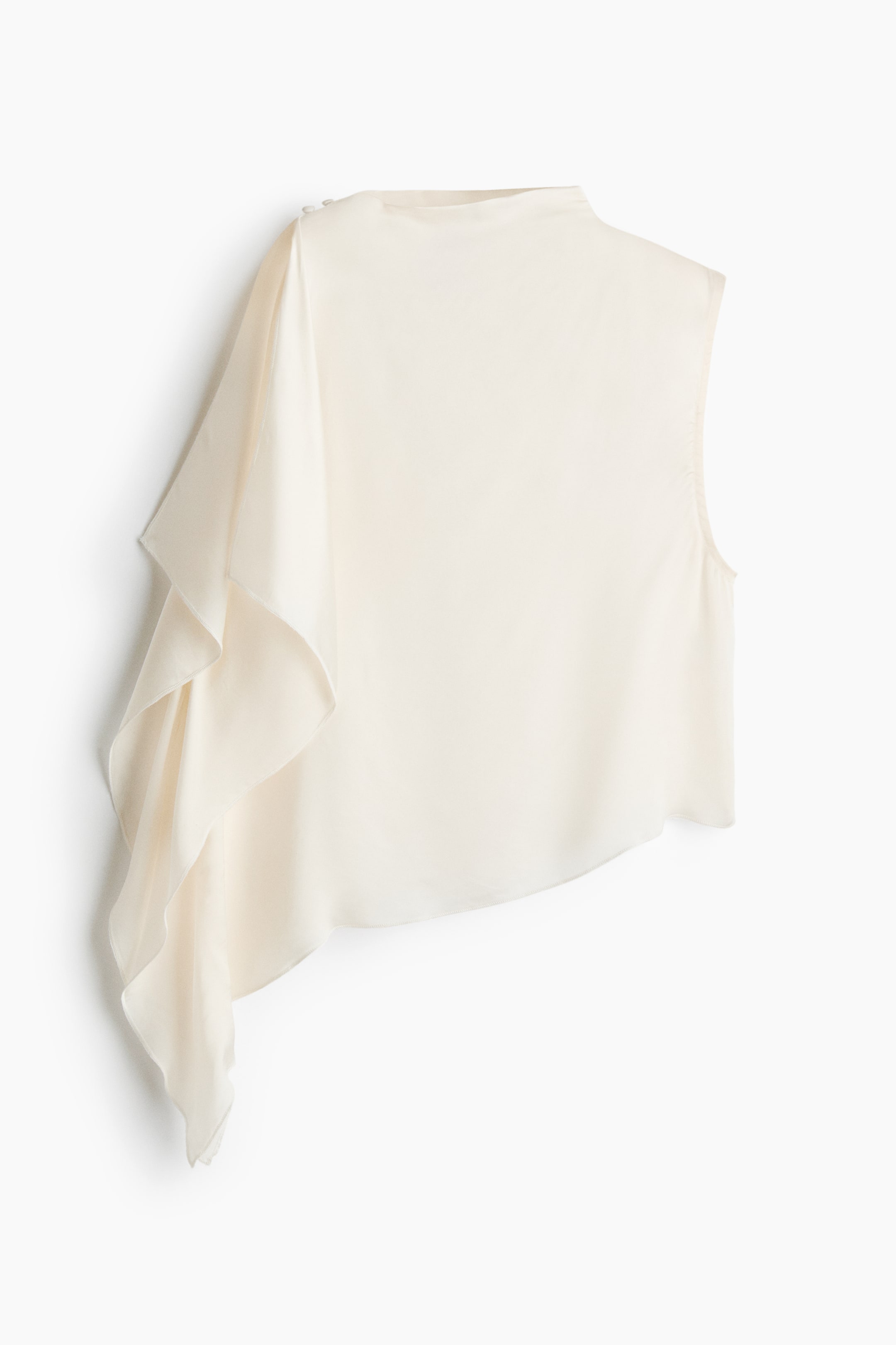 View larger image: A cream sleeveless top features a high neck and an asymmetrical hem, showcased front-facing and slightly angled to the right. A cascading ruffle elegantly drapes down the left side, with small buttons visible on the shoulder.