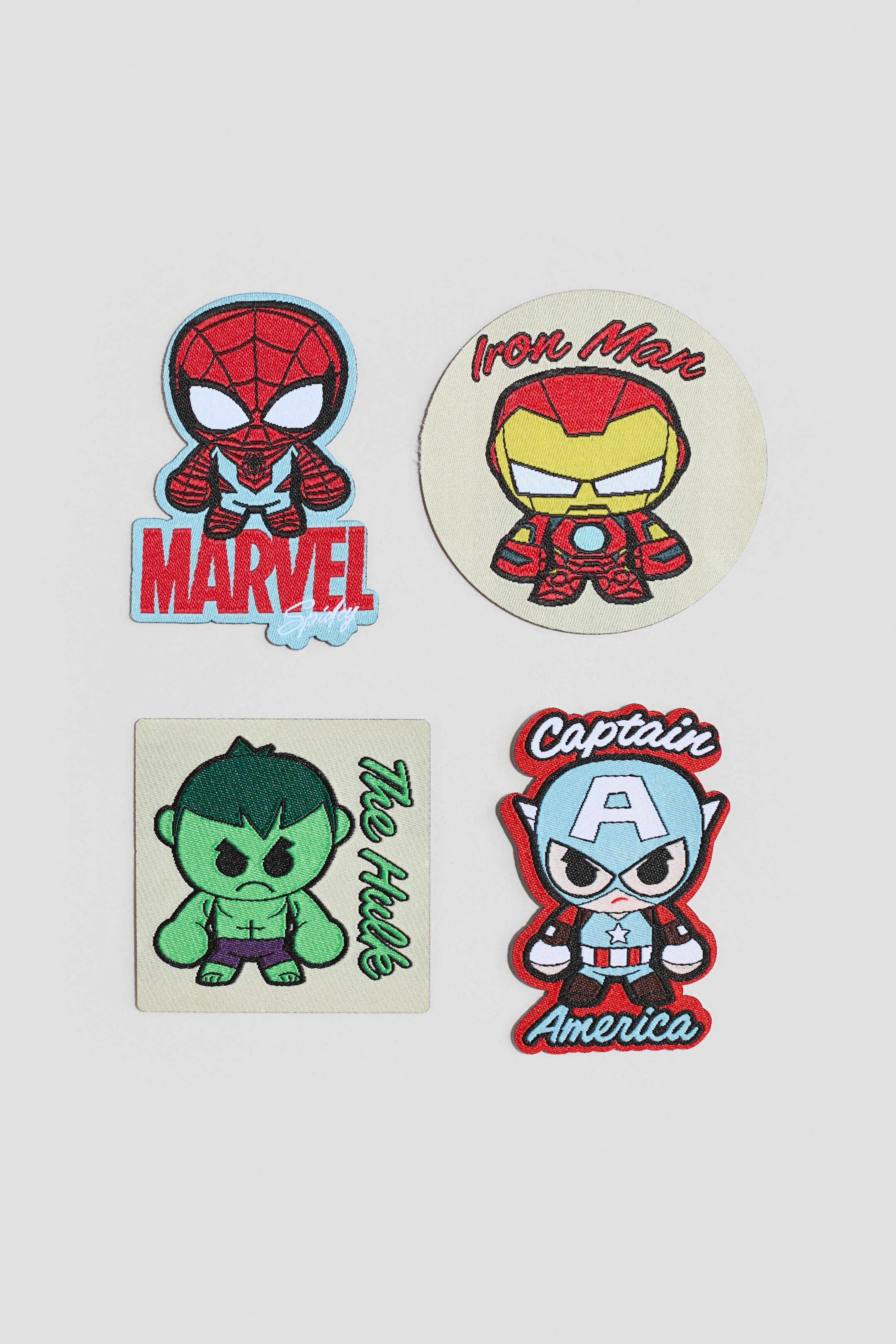 View larger image: A set of four embroidered patches is showing, each featuring a cartoon Marvel character facing front. The patches include an irregularly shaped red and blue Spider-Man with "Marvel" text, a circular beige patch with a red and gold Iron Man and "Iron Man" text, a square beige patch with a green Hulk and "The Hulk" text, and an irregularly shaped blue, red, and white Captain America with "Captain America" text.