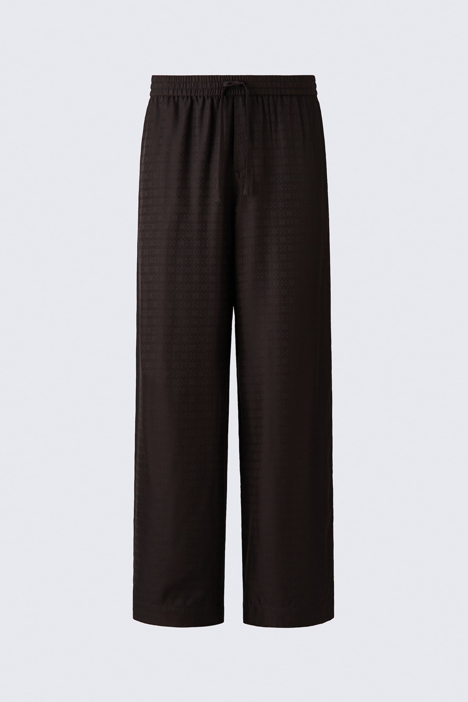 A front view of loose-fit, wide-leg pyjama pants in dark brown, softly draping jacquard satin featuring a subtle all-over monogram pattern. The pants are showcasing an elasticated waistband with a matching drawstring tie and a mock fly.