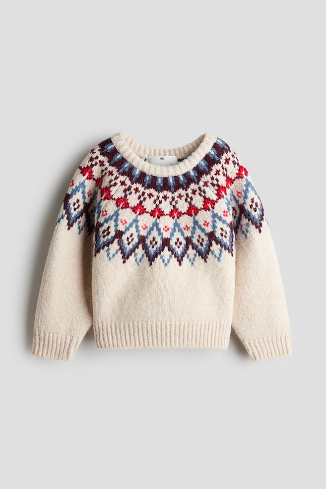 A cream-coloured knit sweater is facing front, displaying a Fair Isle pattern in red, blue, and burgundy around the yoke and upper sleeves. The garment features a ribbed crew neck, ribbed cuffs, and a ribbed hem. - 1