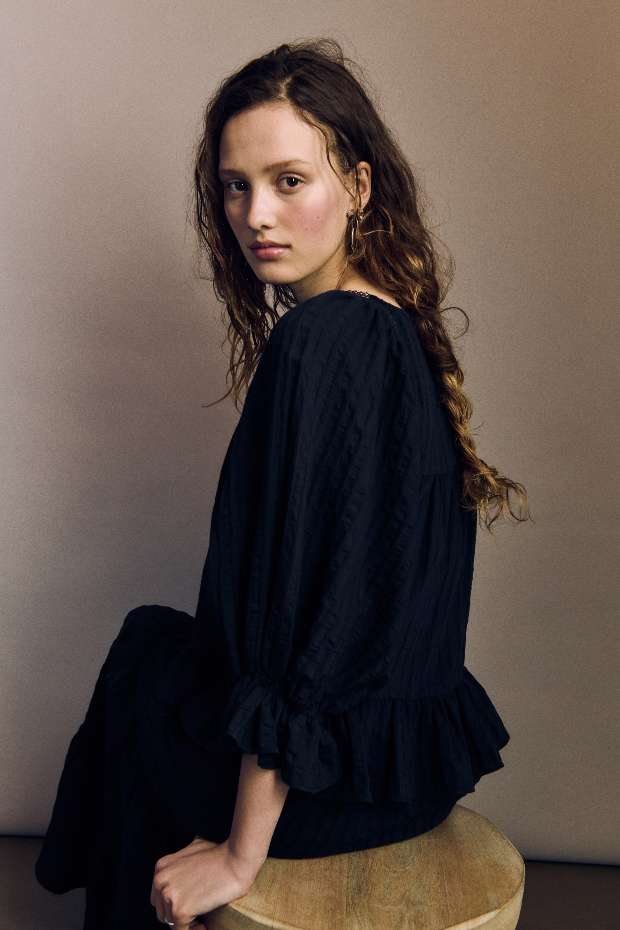 Agrandir l'image: Un chemisier sombre avec un tissage texturé est porté par le mannequin. Il présente un décolleté carré orné de dentelle, des manches bouffantes volumineuses de longueur 3/4 avec des poignets évasés élastiqués, et un large volant à l'ourlet.