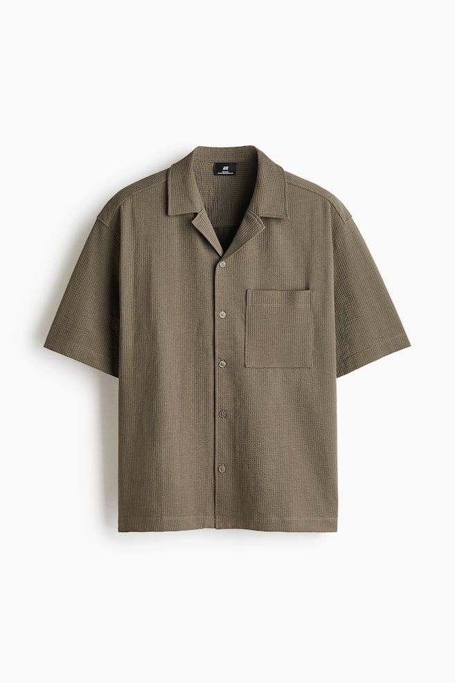 A short-sleeve shirt in a waffled cotton-blend fabric is shown facing the front in a muted olive-brown color. It is featuring a relaxed silhouette with a resort collar, a button-down front, a single open chest pocket, and a straight hem. - 1