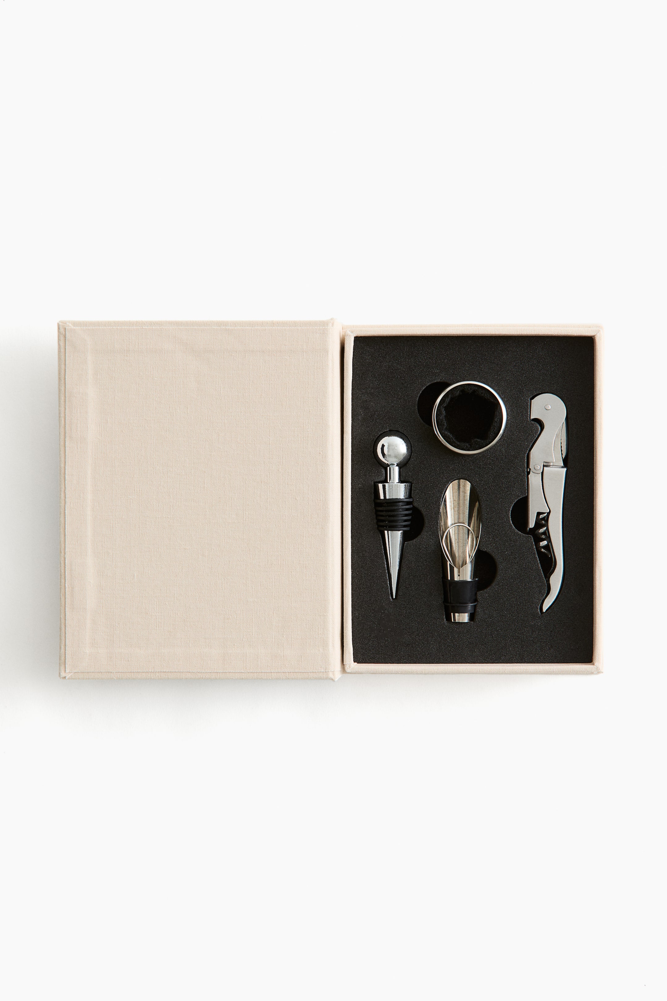 Ver imagem maior: Um conjunto de acessórios para vinho está exposto na FRENTE, numa caixa aberta de cor bege. A caixa apresenta um inserto de espuma preta, que contém um tampão de vinho prateado com uma esfera no topo, um pourer de vinho prateado, um saca-rolhas prateado com um cabo preto e um anel preto.