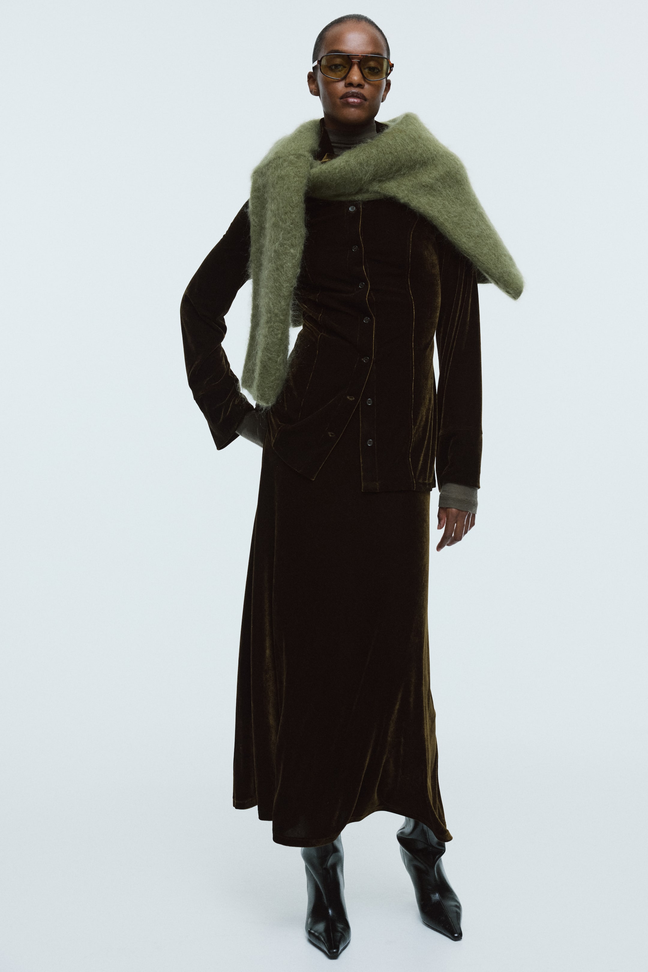 View larger image: A dark olive green velvet button-front shirt-jacket with long sleeves and a matching midi-length skirt are being presented from a slight front-right angle. A fuzzy light olive green scarf is draped over the shoulders, layered over a dark turtleneck, and the ensemble is completed with black pointed-toe boots.